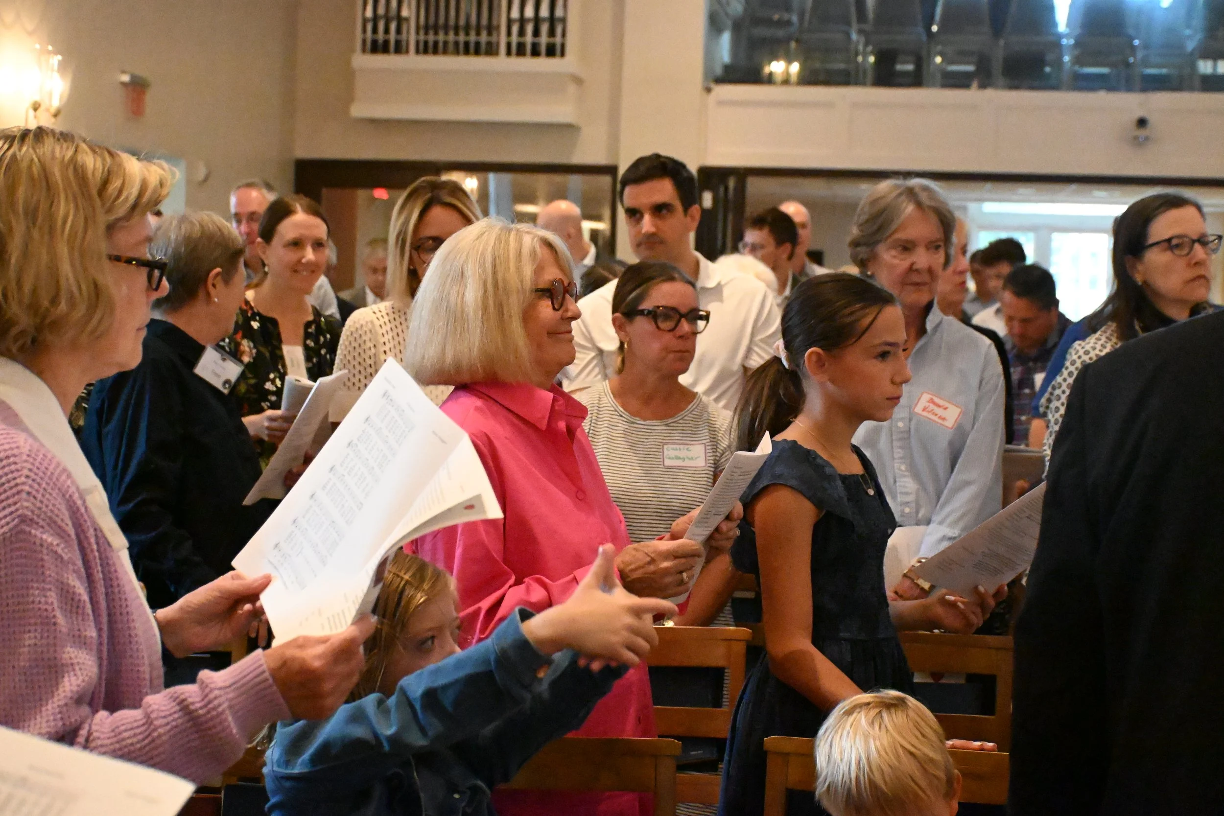 People gathered in a church or chapel, holding hymn books or programs, attending a religious or community service.