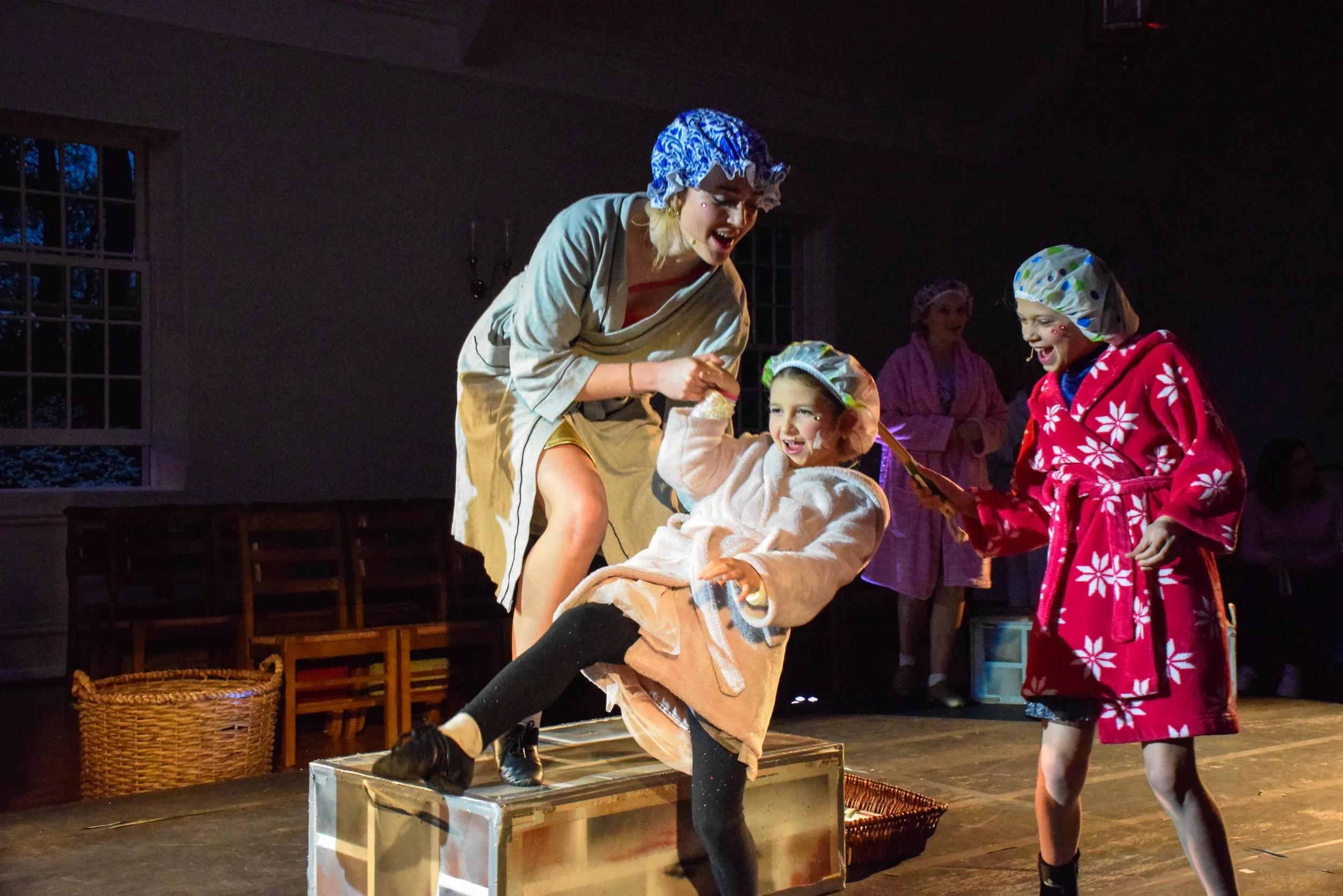 Children and an adult dressed in pajamas and shower caps performing on stage during a play or skit.