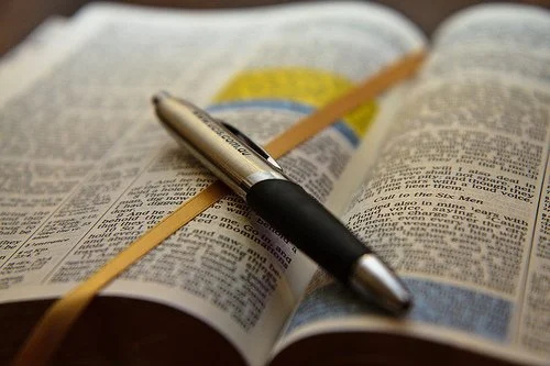 Open book with a black and silver pen and a yellow pencil resting on the pages.