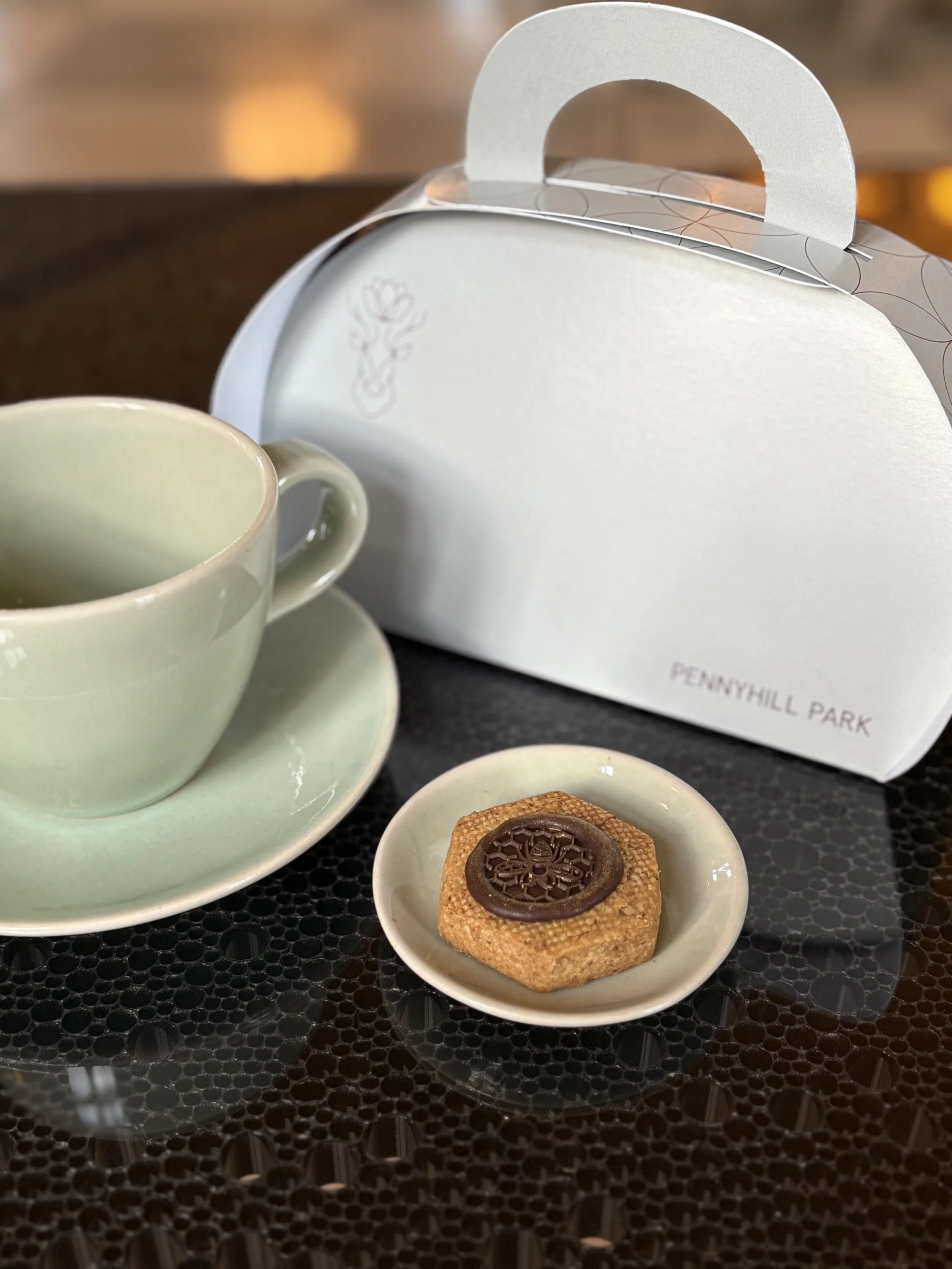 Image of a biscuit, cup and saucer and a takeaway afternoon tea box.