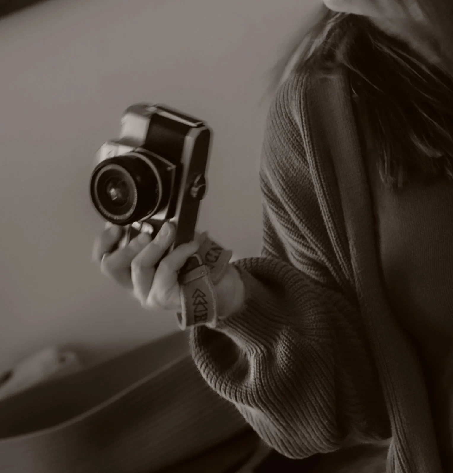 A person taking a mirror selfie with a vintage camera, wearing a striped sweater and a glove on one hand.