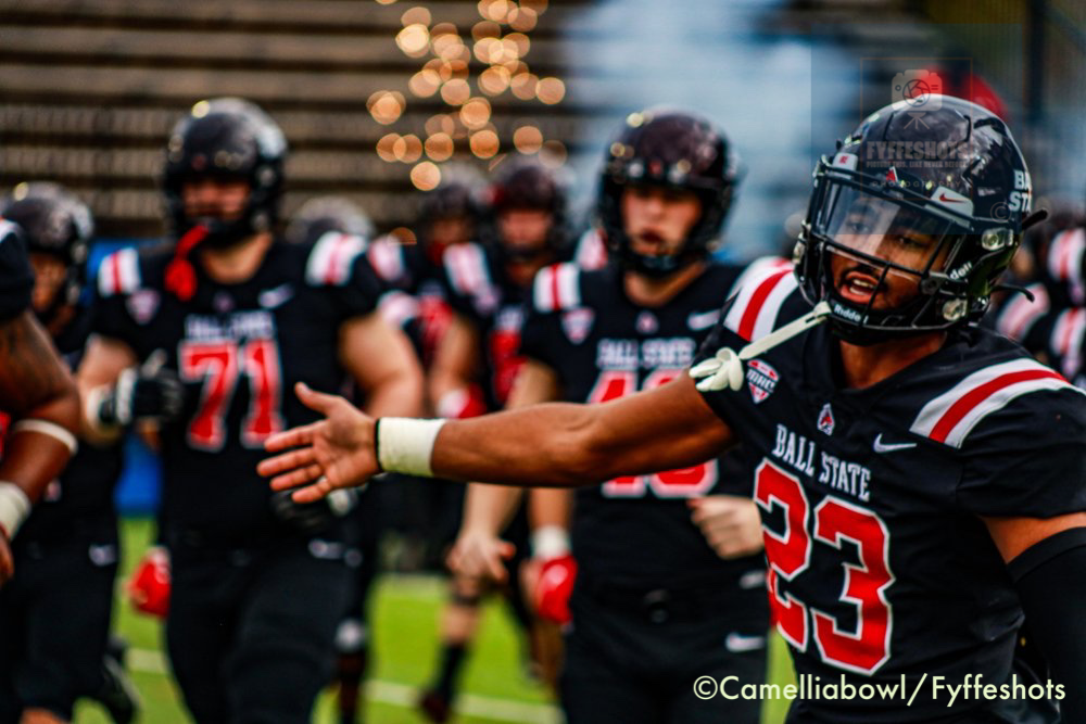 Ball State football player wearing number 33 jersey and helmet gestures toward teammates on the field.