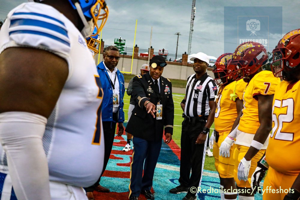 Military officer and referee meet with football players on a field before a game