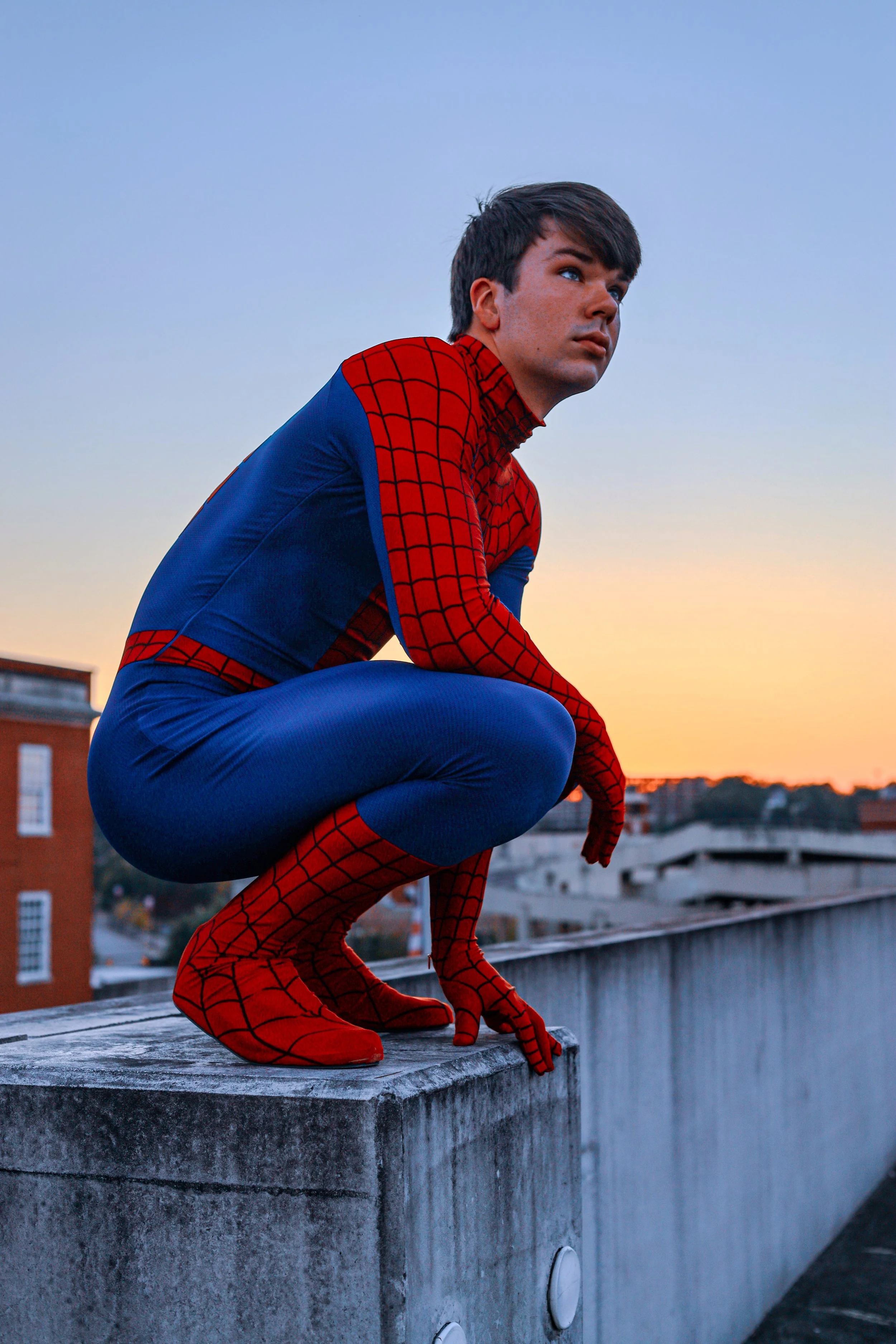 Person in a Spider-Man costume crouching on a rooftop at sunset