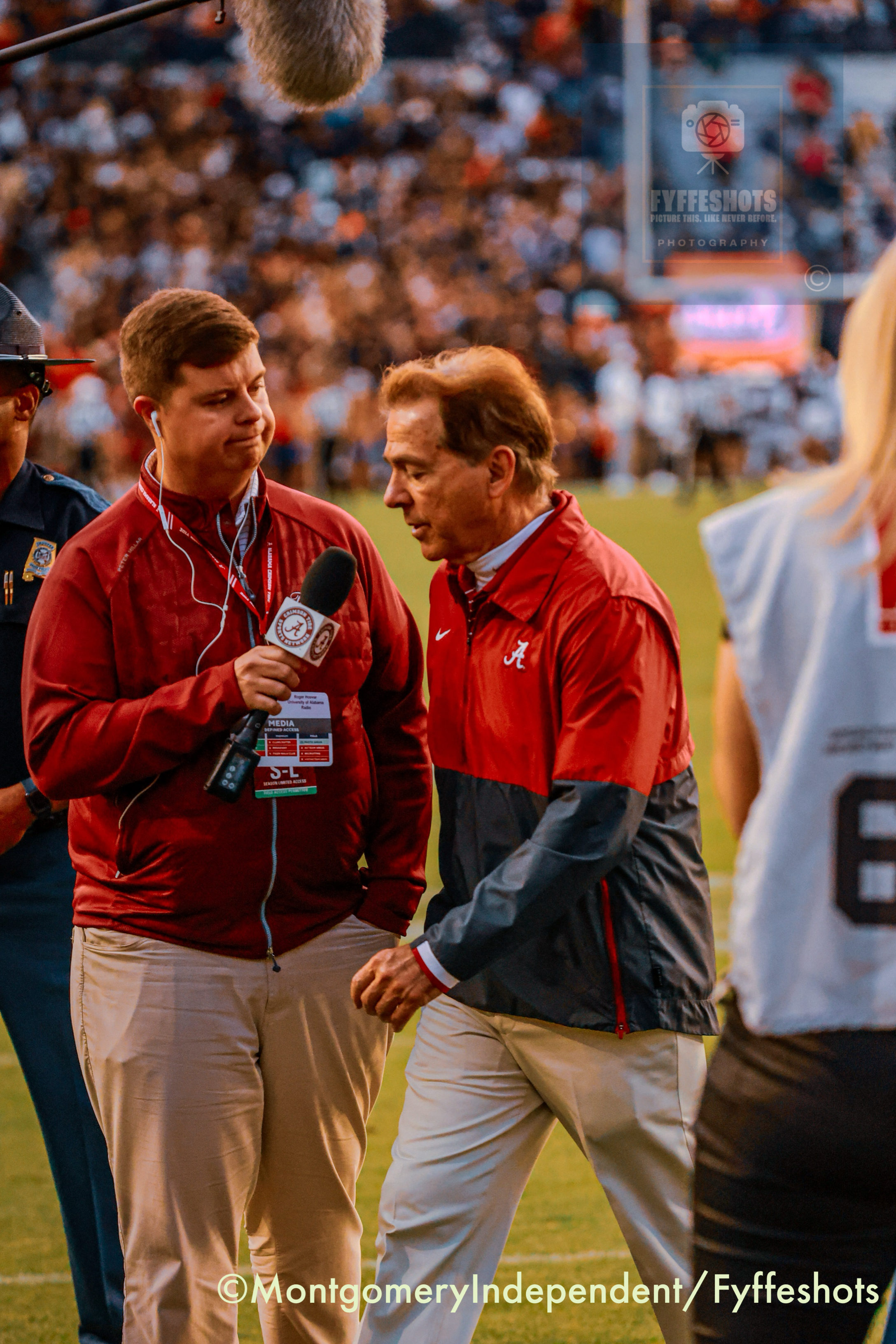 Alabama football coach Nick Saban speaks with a University of Alabama radio reporter on the field during a game.