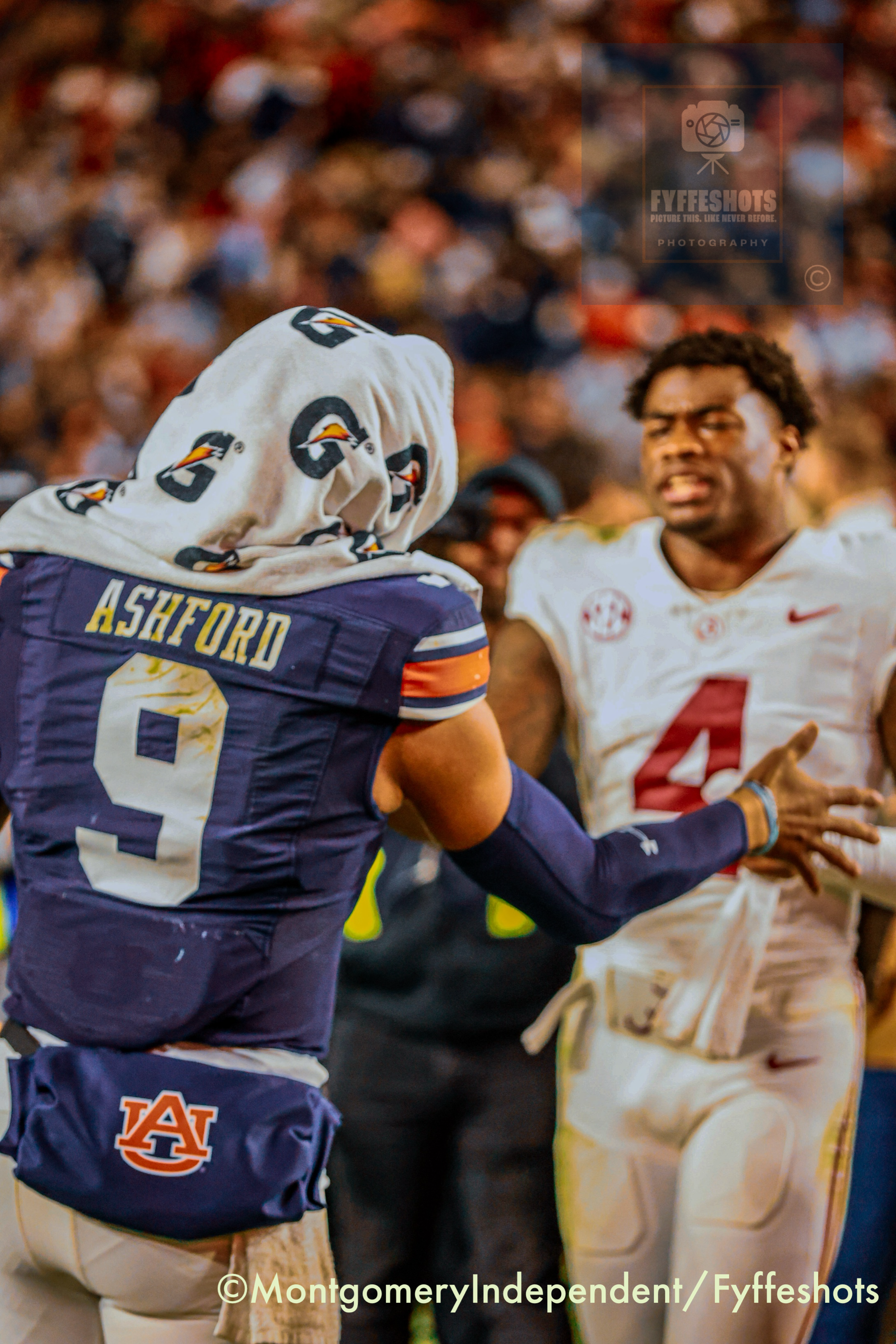 Auburn Tigers football players in navy and white uniforms celebrate on the field with a blurred crowd behind them.
