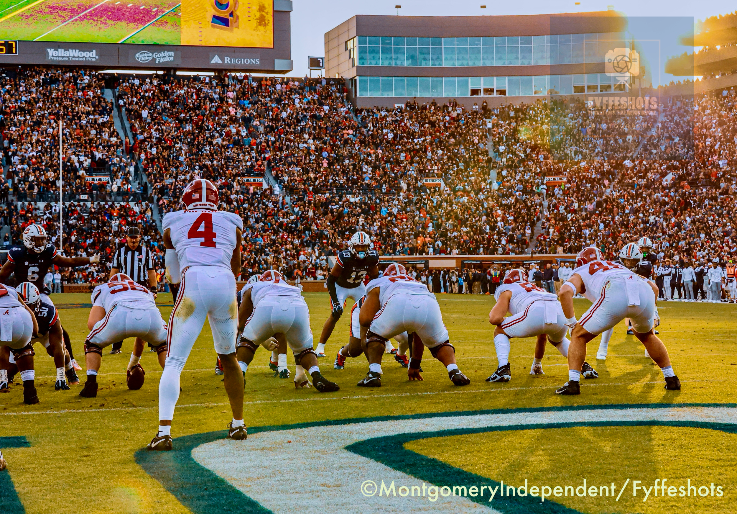 Alabama Crimson Tide football players line up against the Auburn Tigers before a play in a packed college stadium.