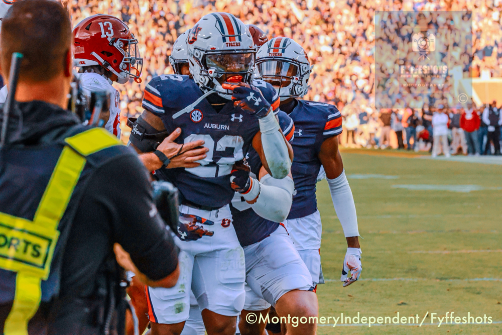 Auburn Tigers football players celebrate on the field during a game, with a sideline photographer in the foreground.