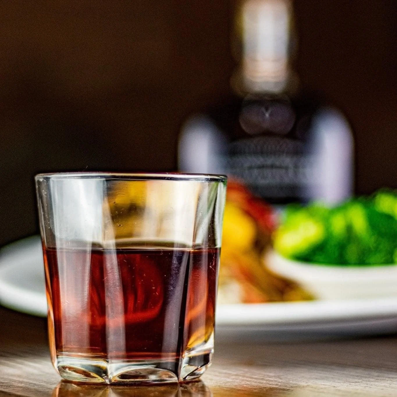 Glass of red wine beside a plate of vegetables and a wine bottle
