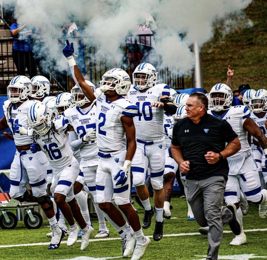 Georgia State Panthers football players and coach run onto the field through smoke before a game.