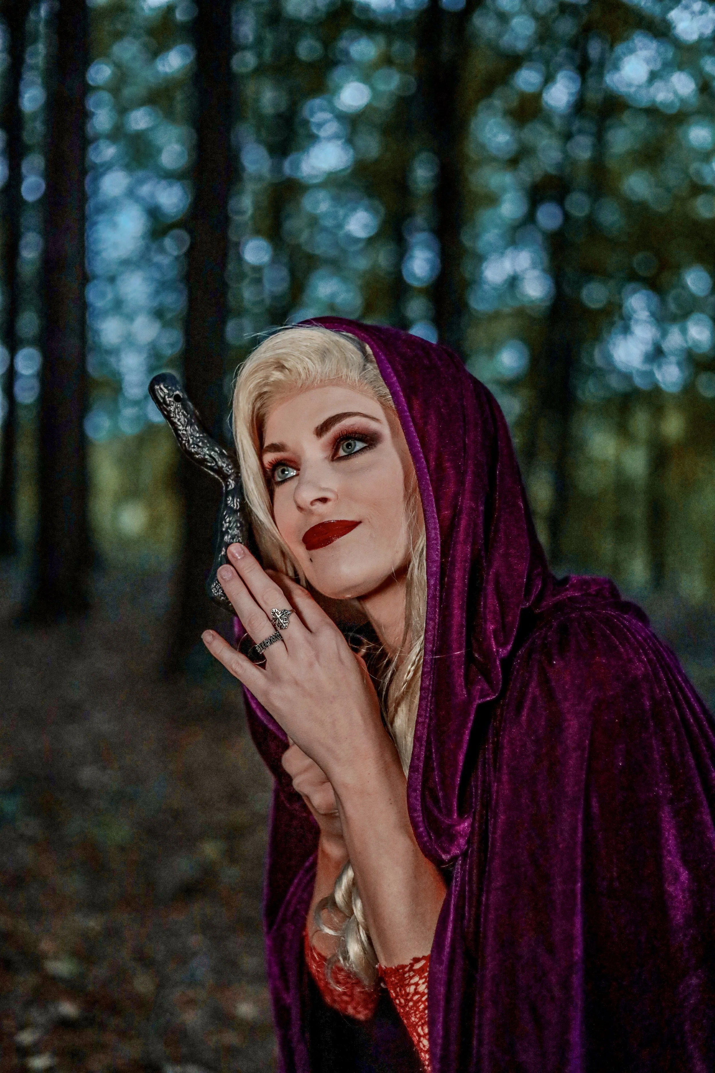Blonde woman in a purple hooded cloak holding an ornate black staff in a misty forest