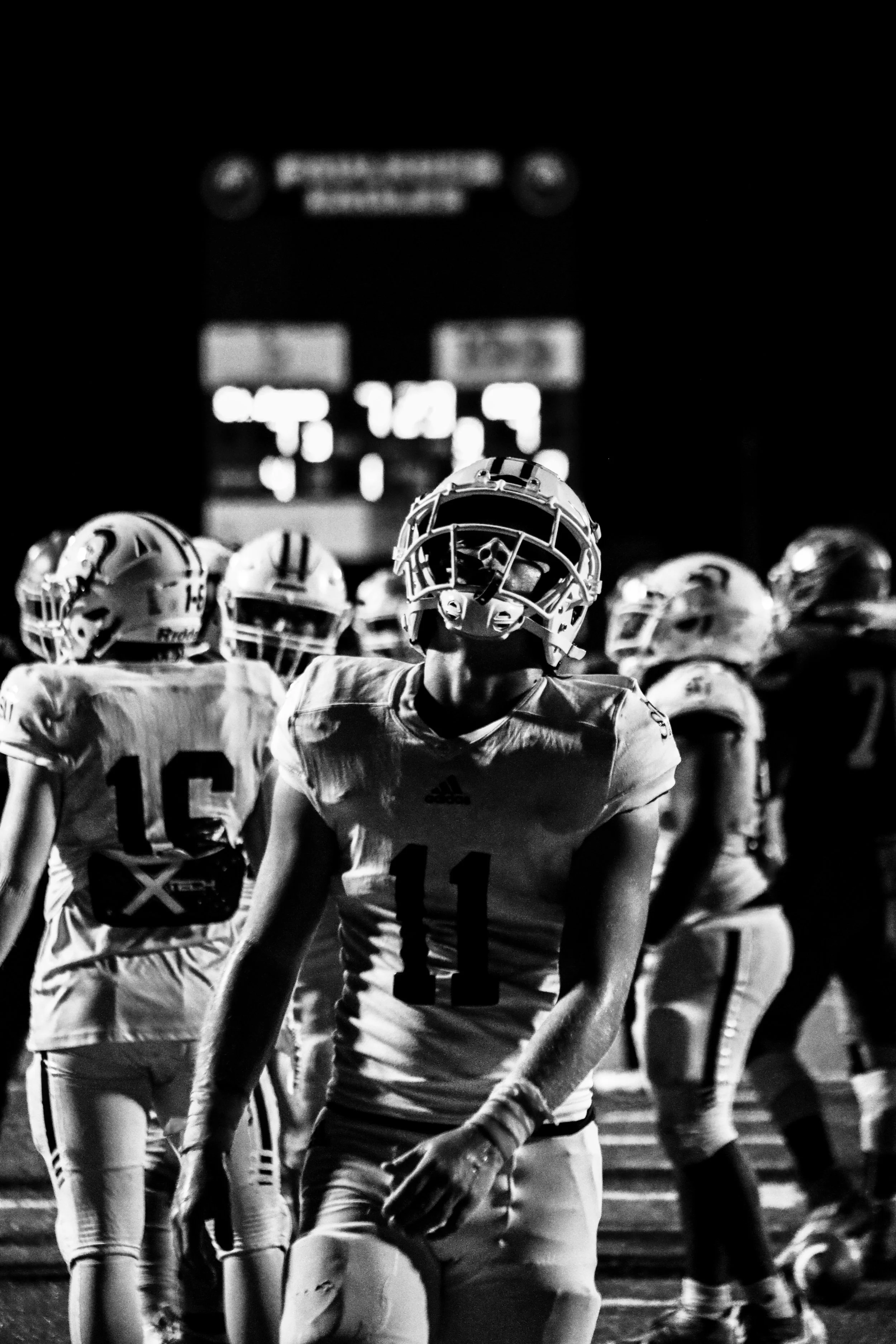 Black-and-white photo of football players lined up on the field beneath a scoreboard.