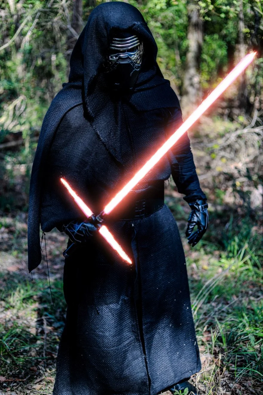 Cosplayer dressed as Kylo Ren holding two glowing red lightsabers in a forest