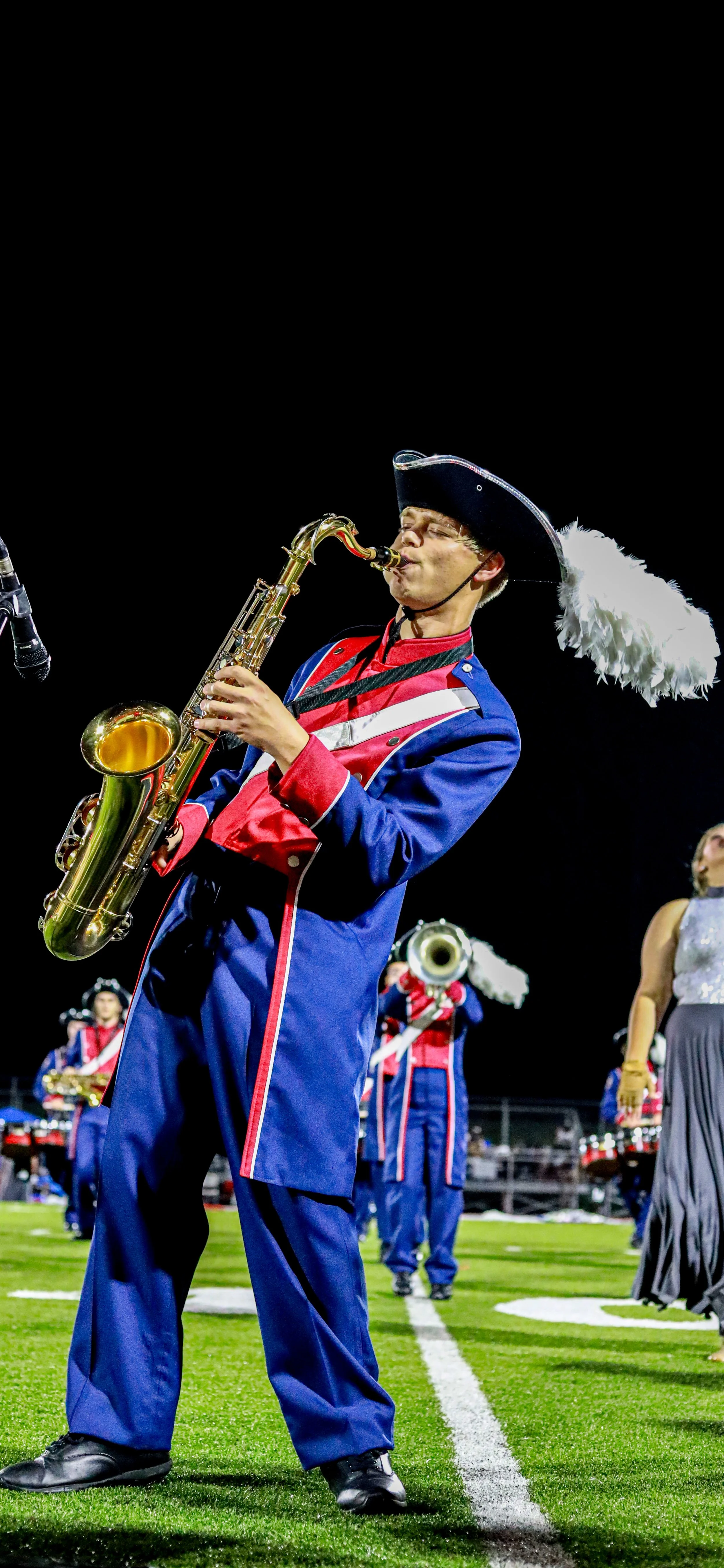 Marching band saxophonist in a blue and red uniform performing on a football field