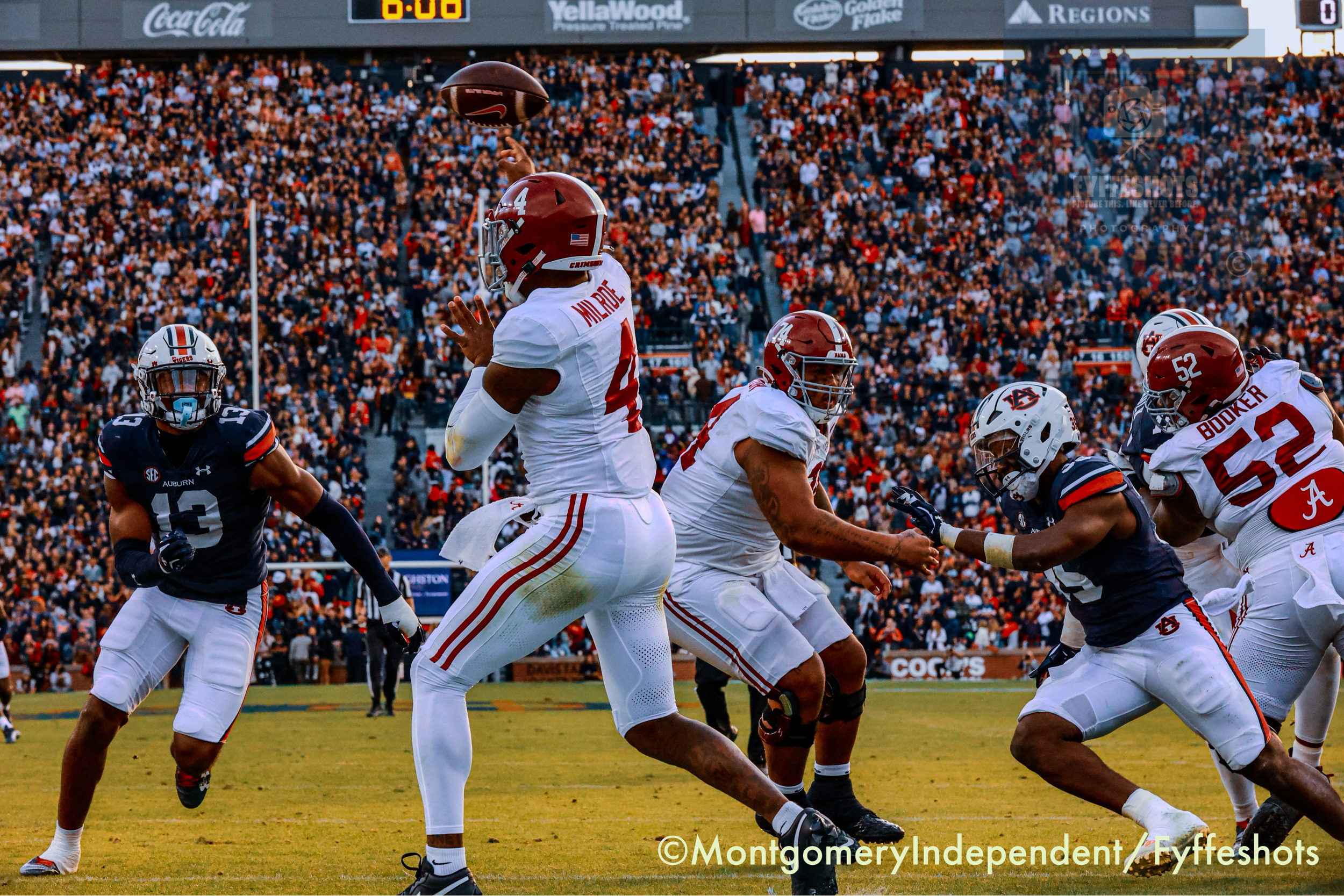 Alabama Crimson Tide quarterback throws a football against Auburn Tigers defenders during a packed college football game.