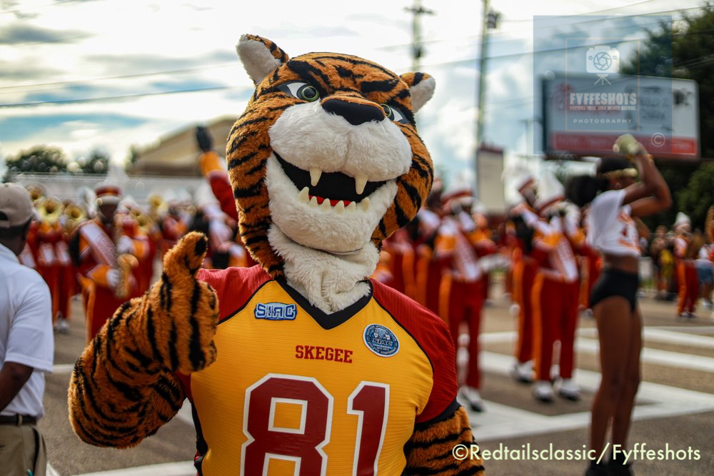 Tiger mascot in a Skegee football jersey posing with a marching band at a parade
