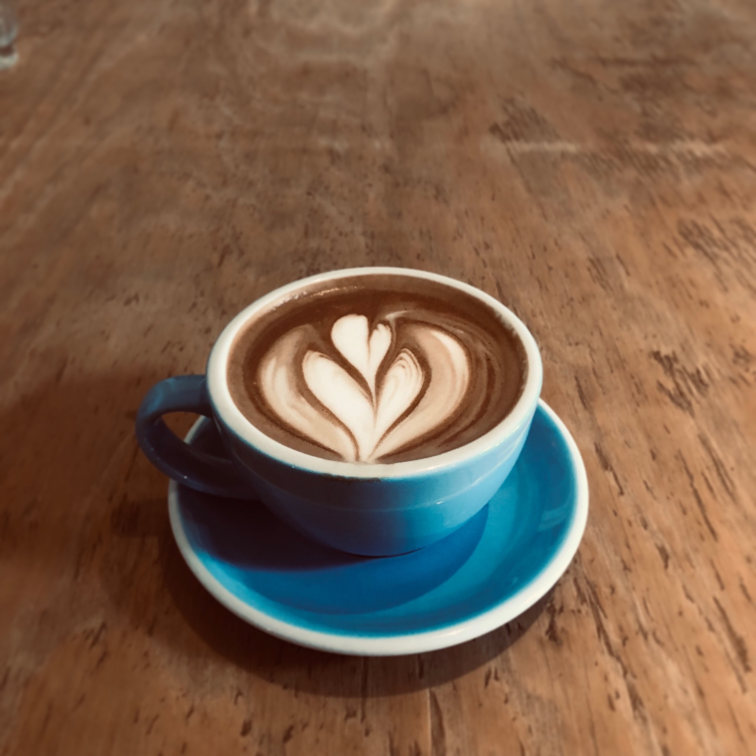 Blue ceramic cup of latte with heart-shaped foam art on a wooden table