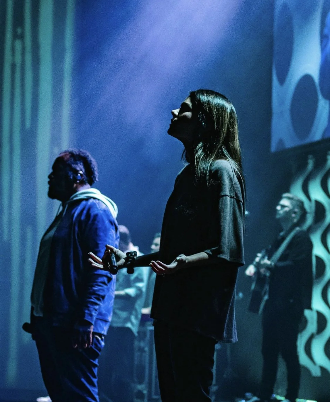 Musicians performing onstage under blue and teal lighting, with a female singer holding a microphone in the foreground.