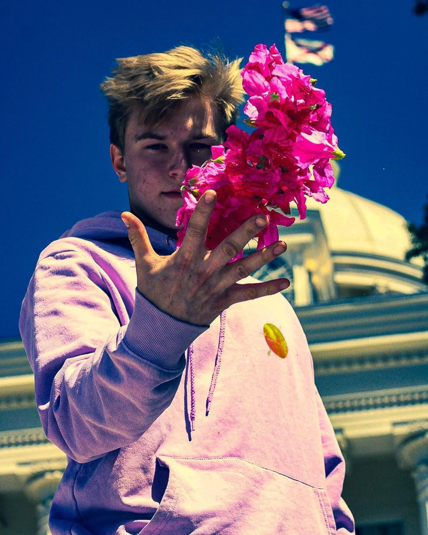 Young man in a pink hoodie holding a large cluster of bright pink bougainvillea flowers in front of his face
