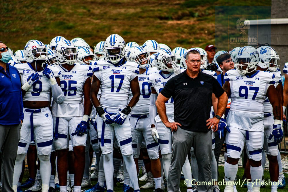 Georgia State football players in white uniforms standing with their coach on the sideline