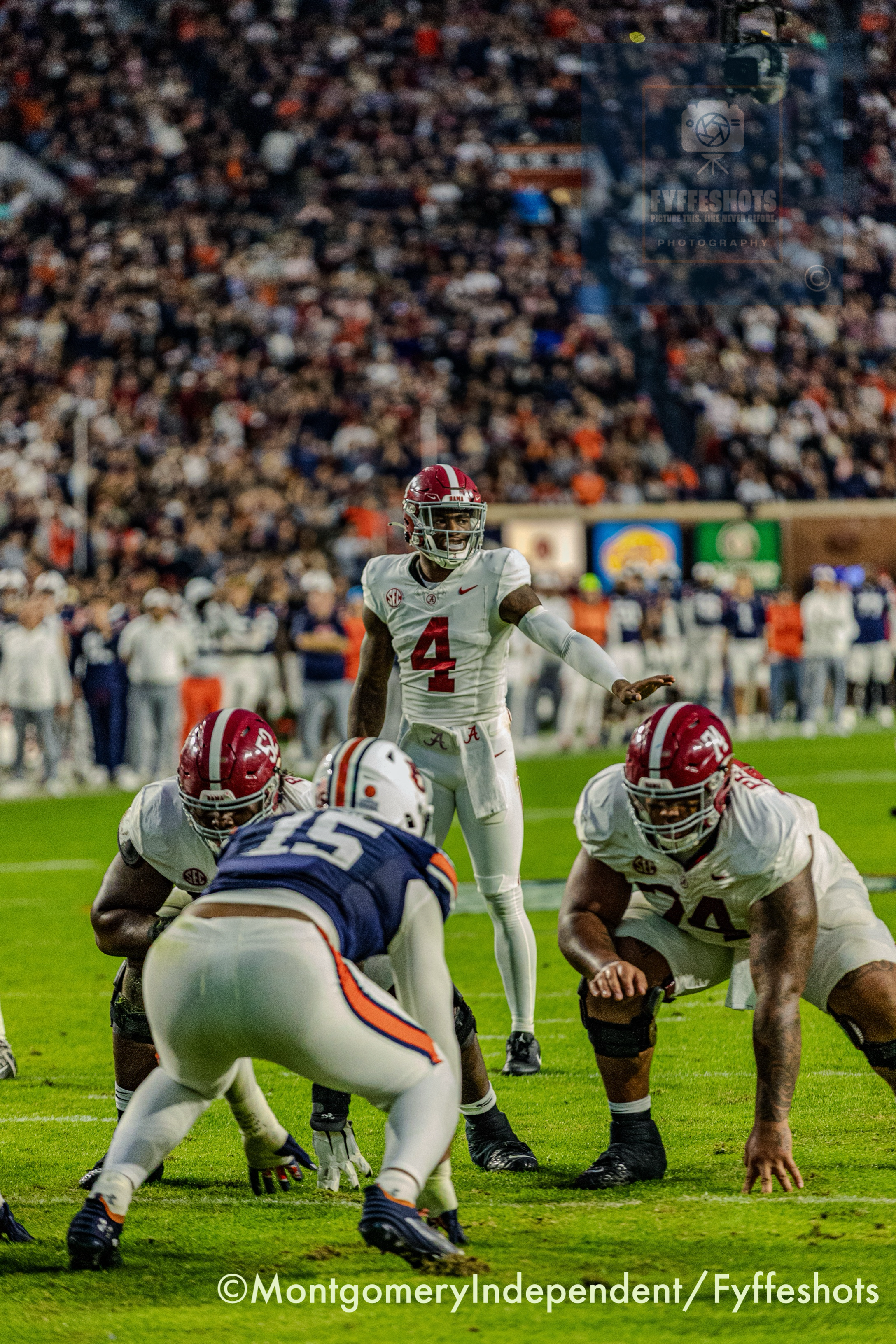 Alabama football quarterback Jalen Milroe in a white No. 4 jersey scrambles against Auburn defenders on a crowded field.