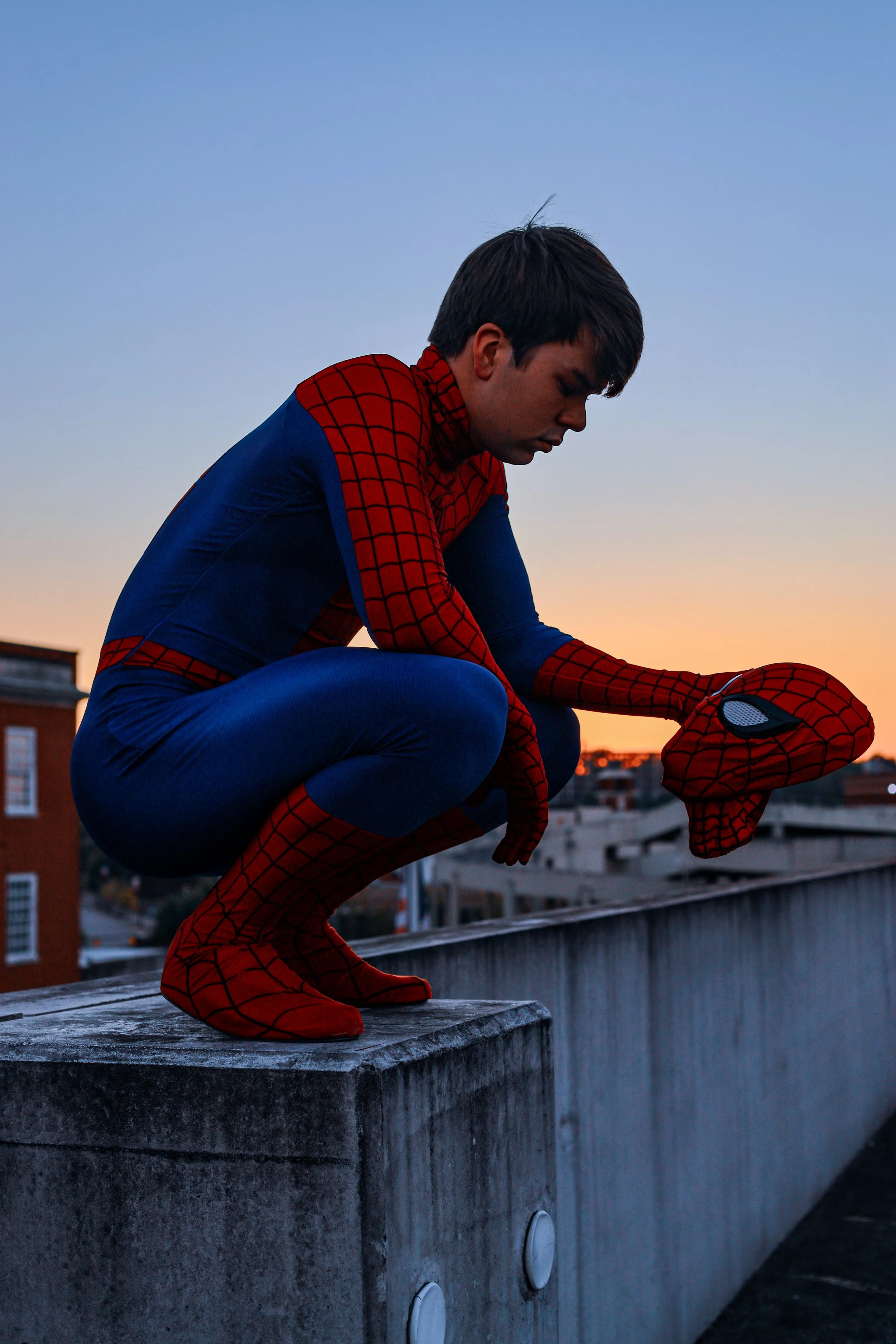 Person in a Spider-Man costume crouching on a rooftop at sunset