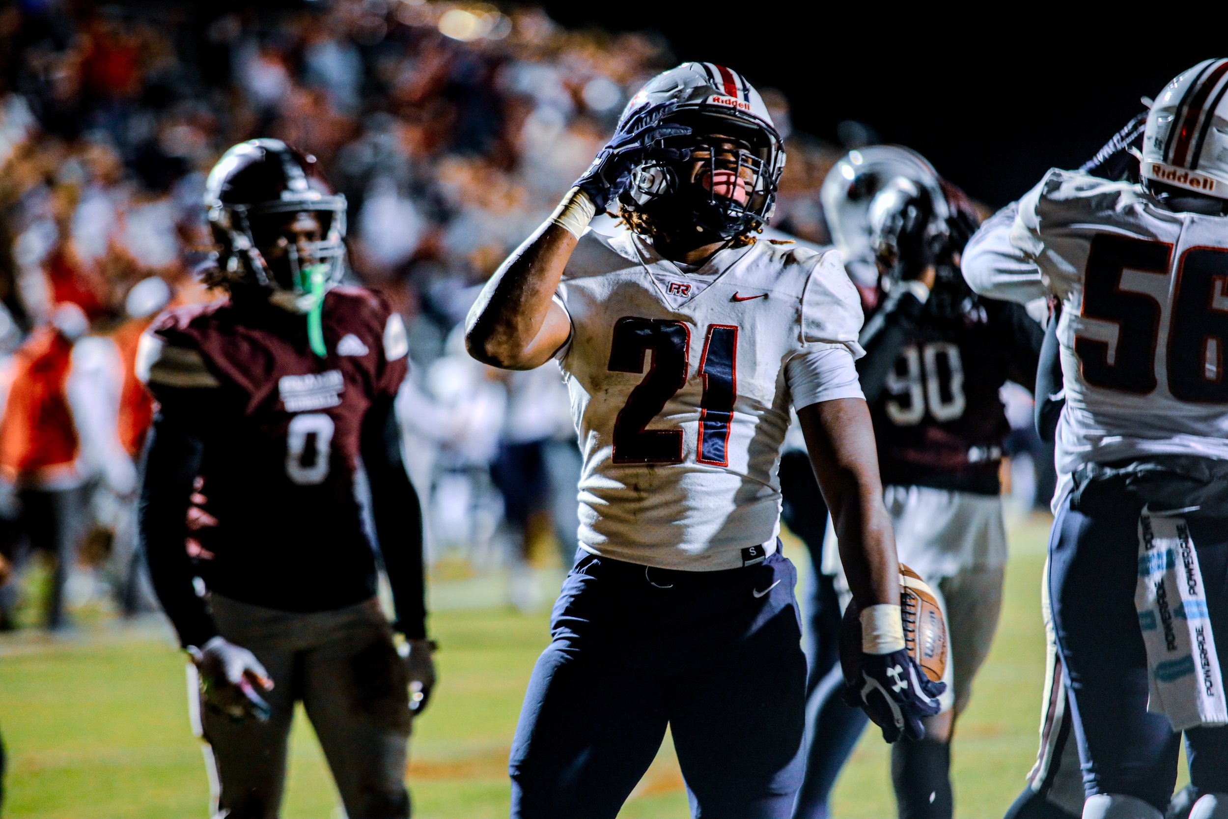 College football player in a white No. 21 jersey and helmet signaling on the field during a nighttime game