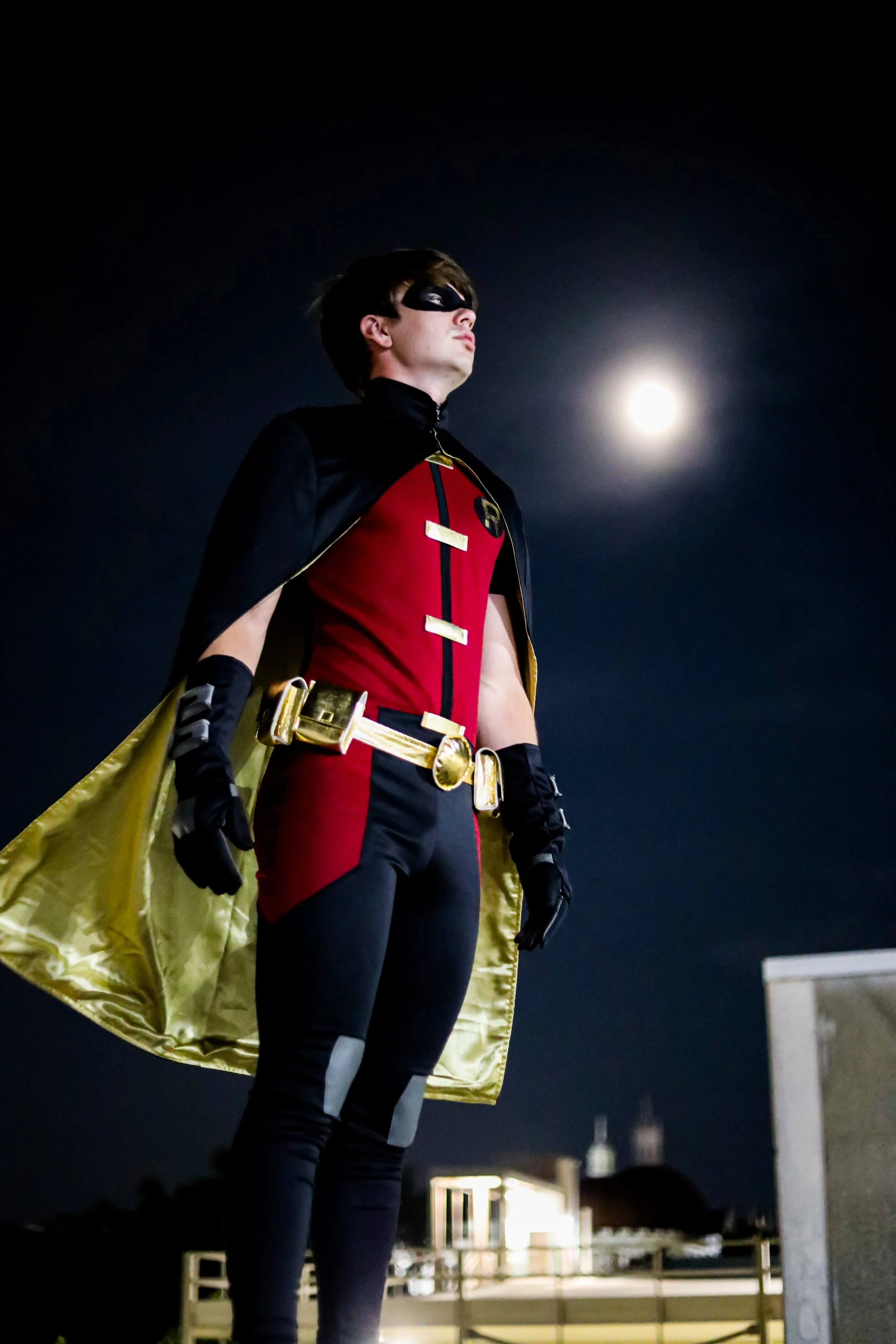 Person dressed as a masked superhero in a red and black costume with a gold cape and sword