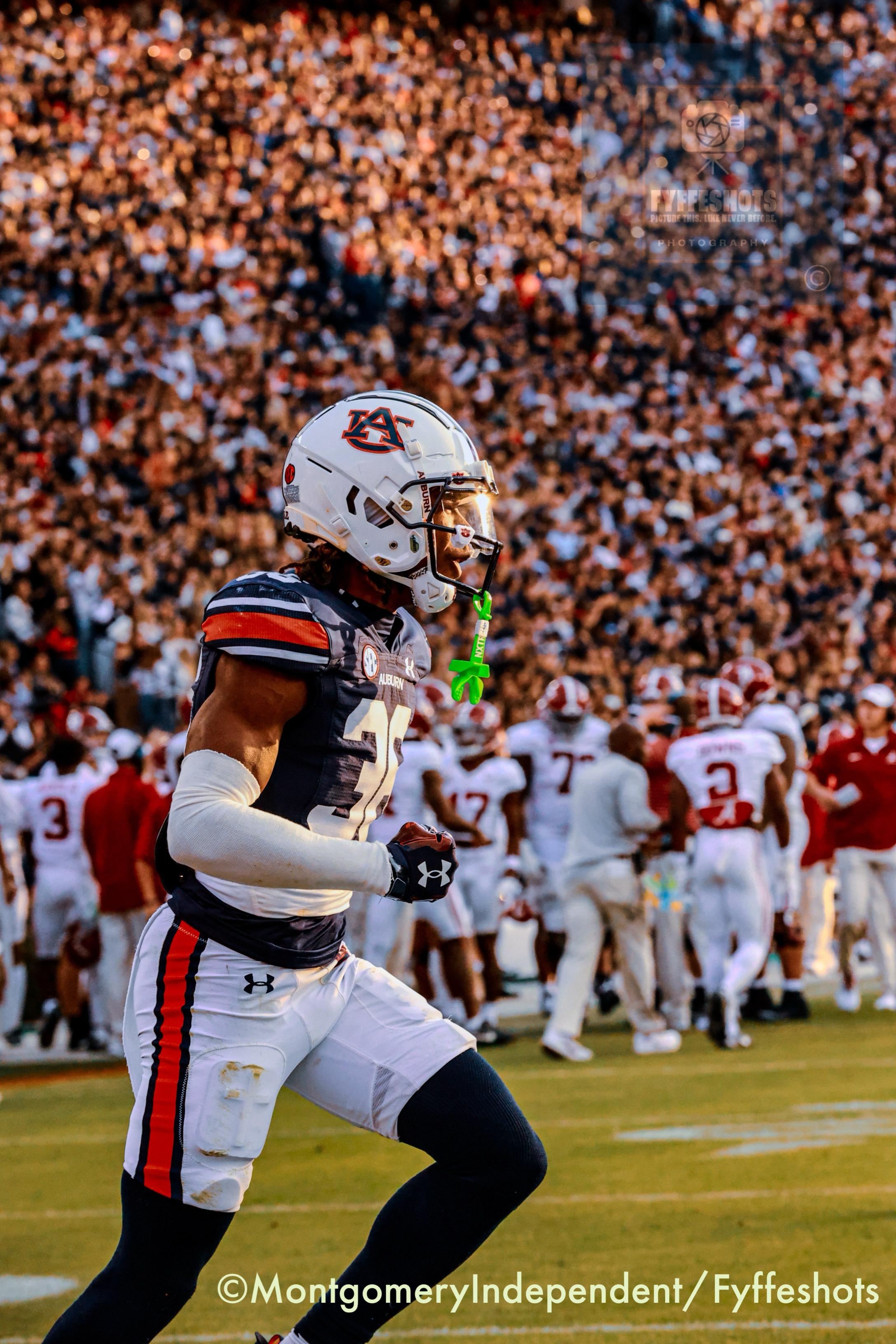 Auburn football player wearing a white helmet and navy-orange uniform celebrates before a packed stadium crowd.