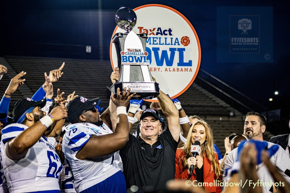 College football team celebrates winning the TaxAct Camellia Bowl while holding the championship trophy.