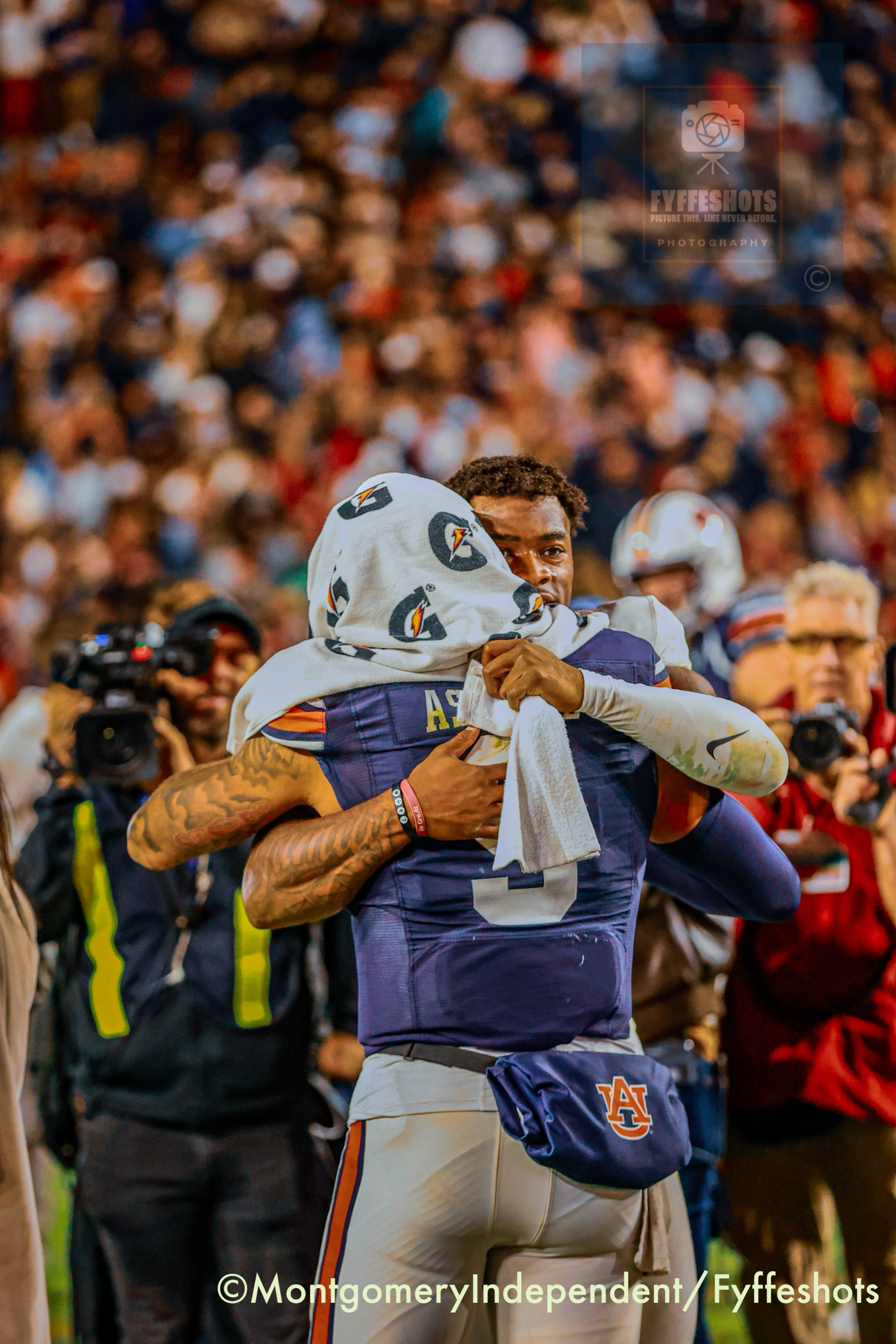 Auburn football player carries a teammate through a cheering crowd after a game.