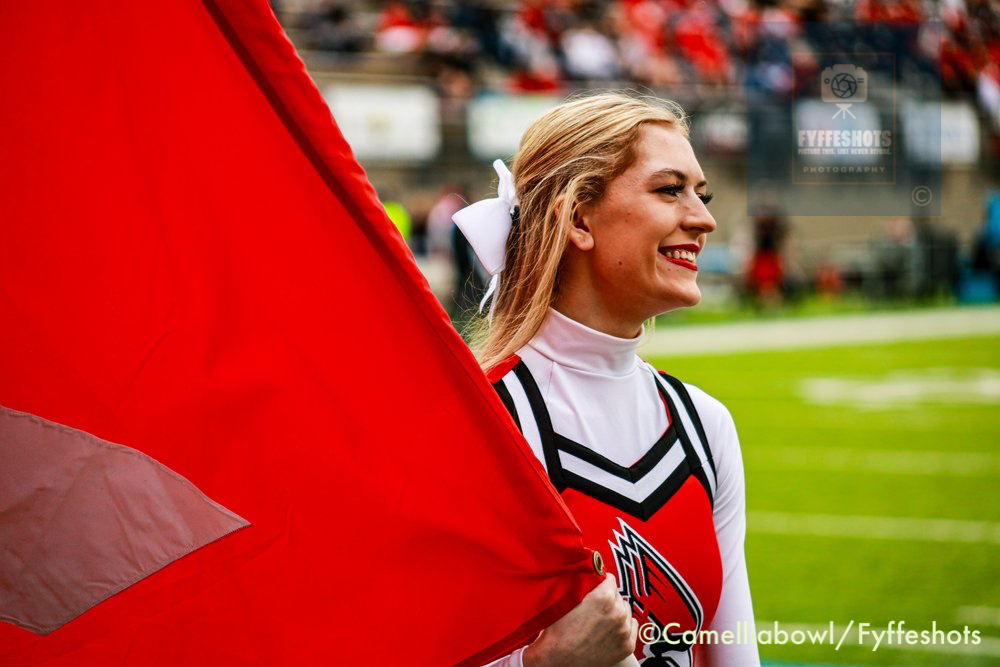 Smiling cheerleader holding a large red flag on a football field