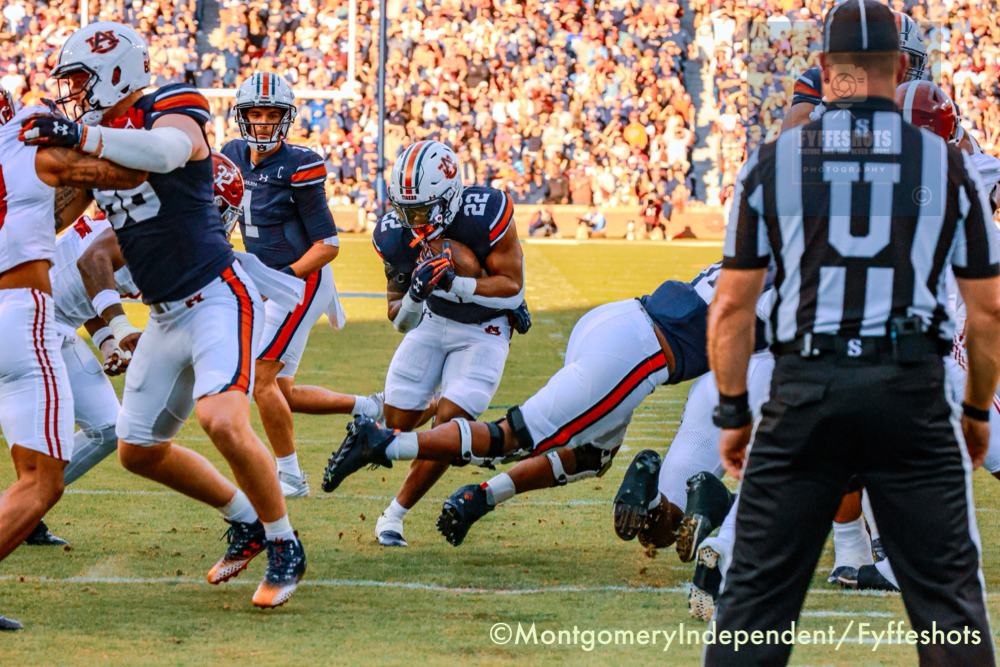 Auburn Tigers football players run a play against Alabama as a ball carrier advances with the football.