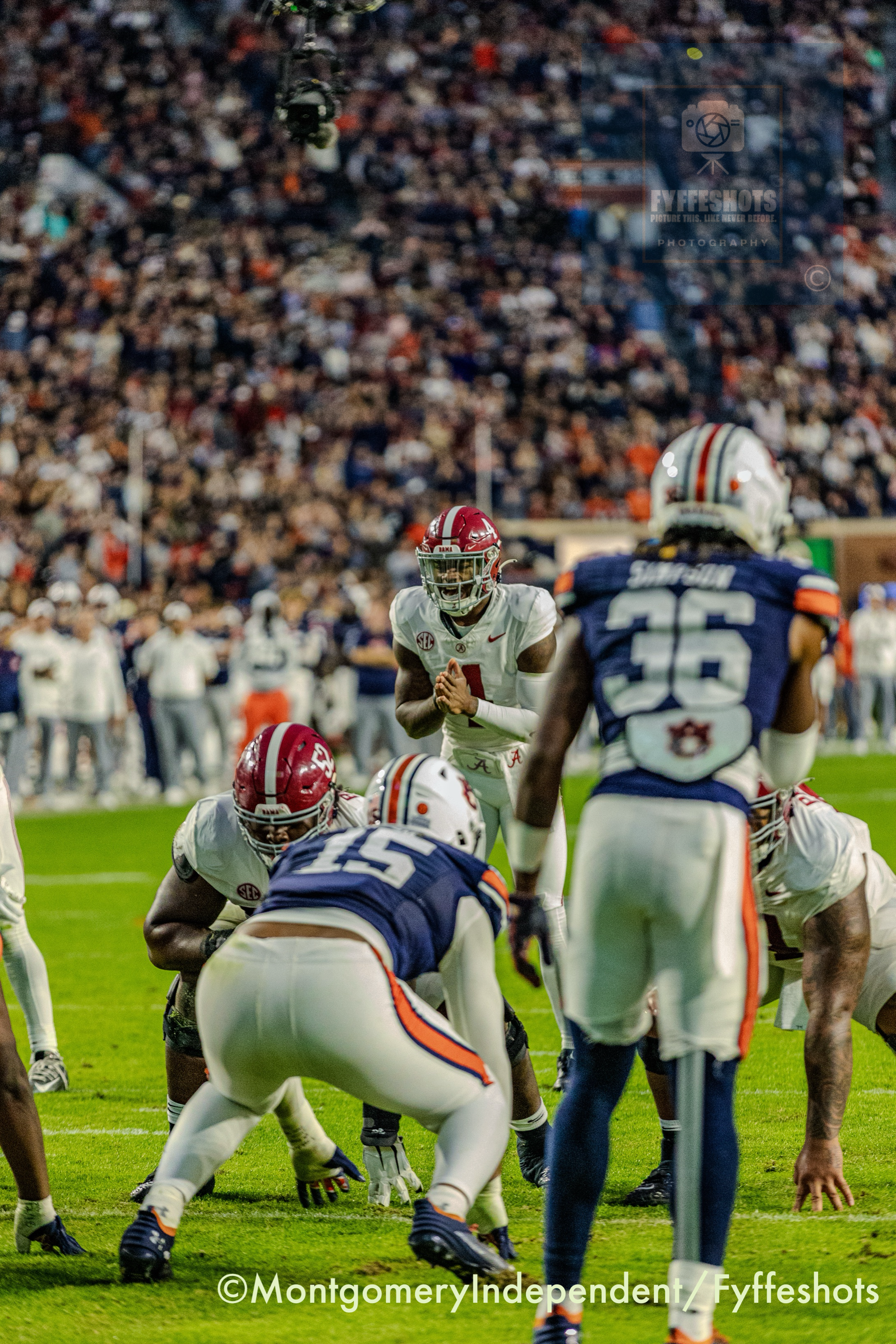 Alabama quarterback faces Auburn defenders during a college football game at a crowded stadium.