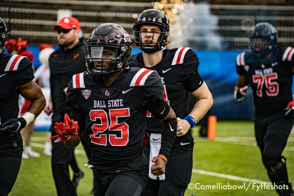 Ball State football players in black and red uniforms running onto the field, led by player number 25.