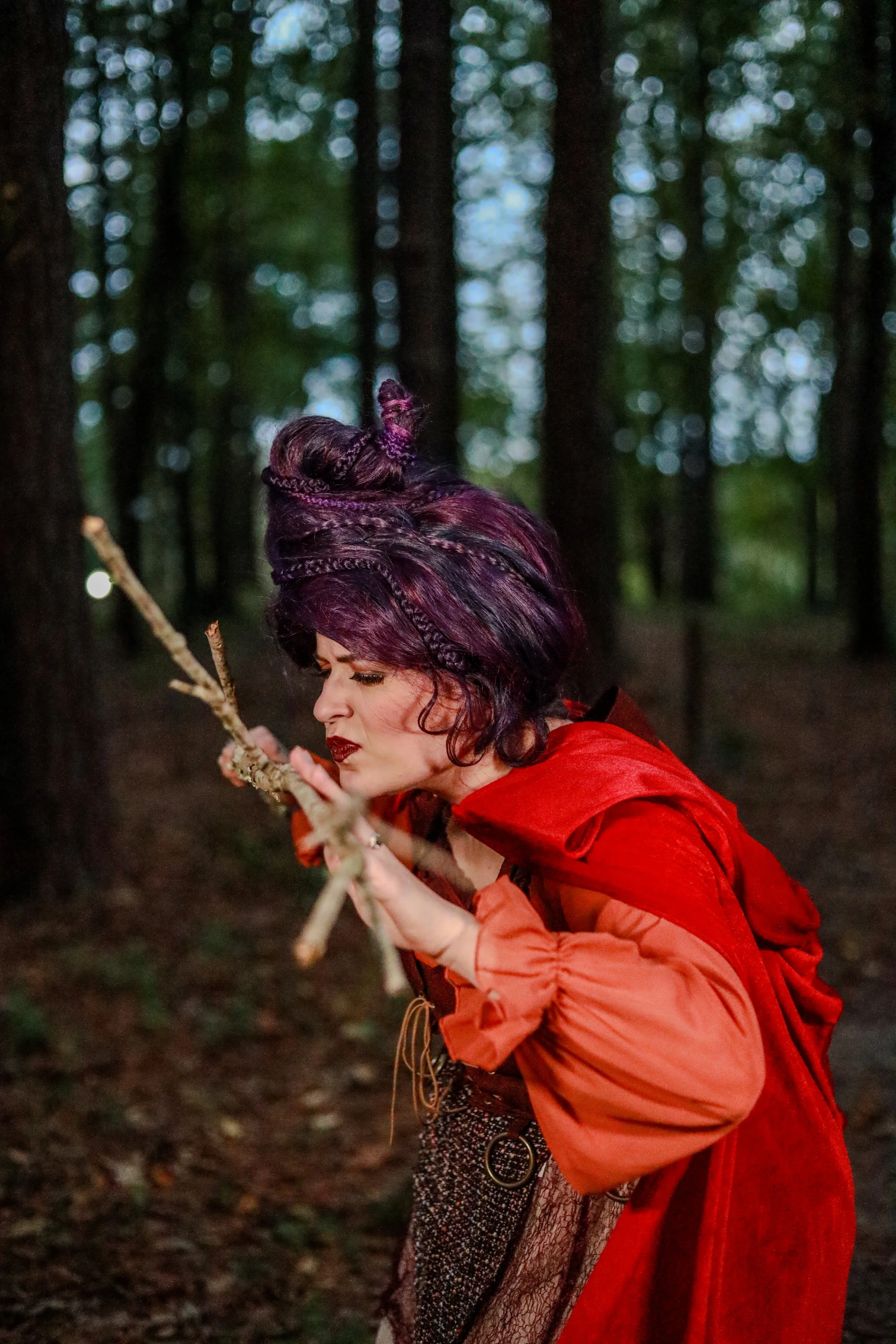 Woman in a red cloak with braided dark hair holding a wooden staff in a misty forest