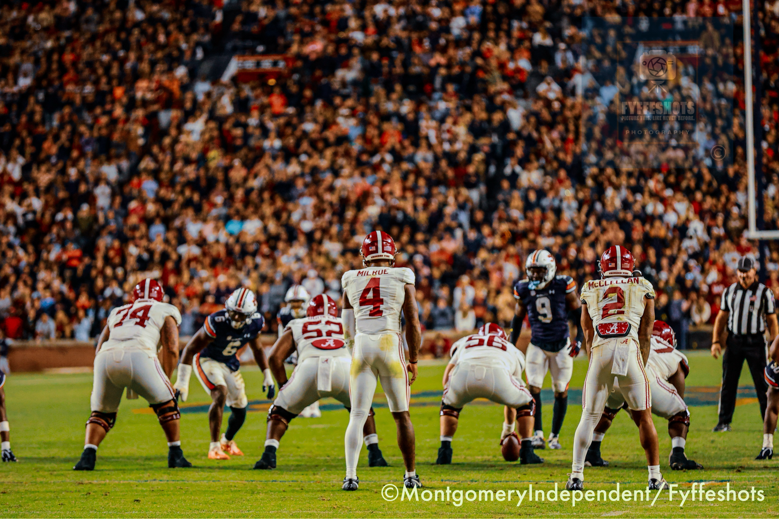 Alabama Crimson Tide football players line up against Auburn Tigers players before a play in front of a packed stadium.