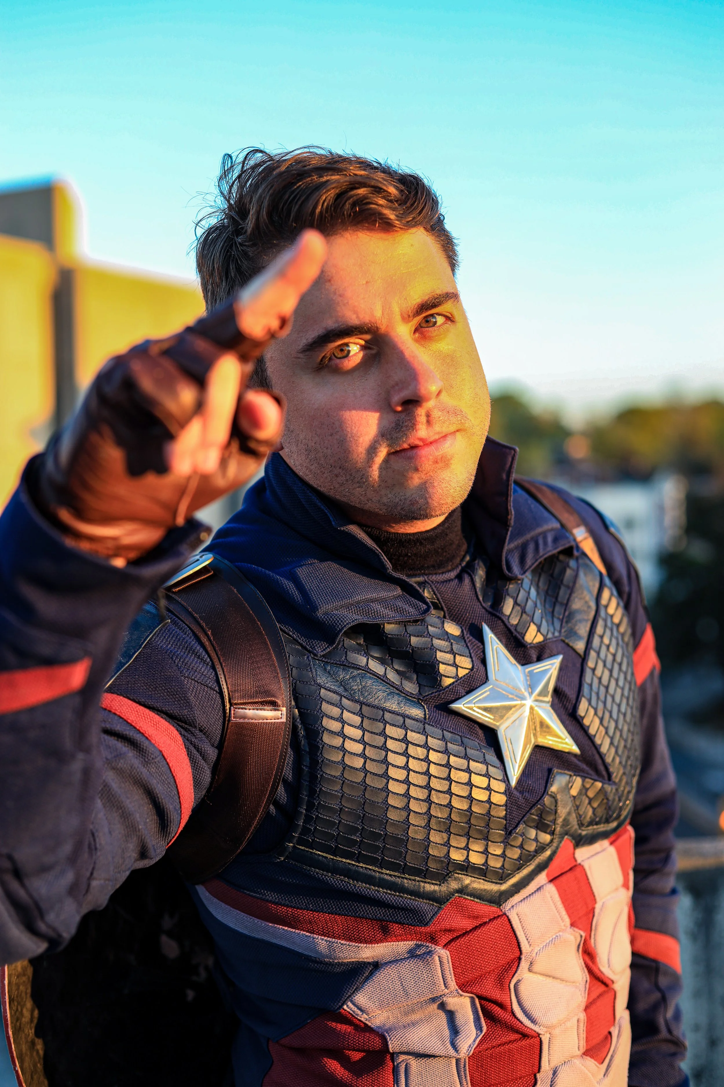 Close-up of a smiling man in futuristic superhero armor pointing toward the camera outdoors