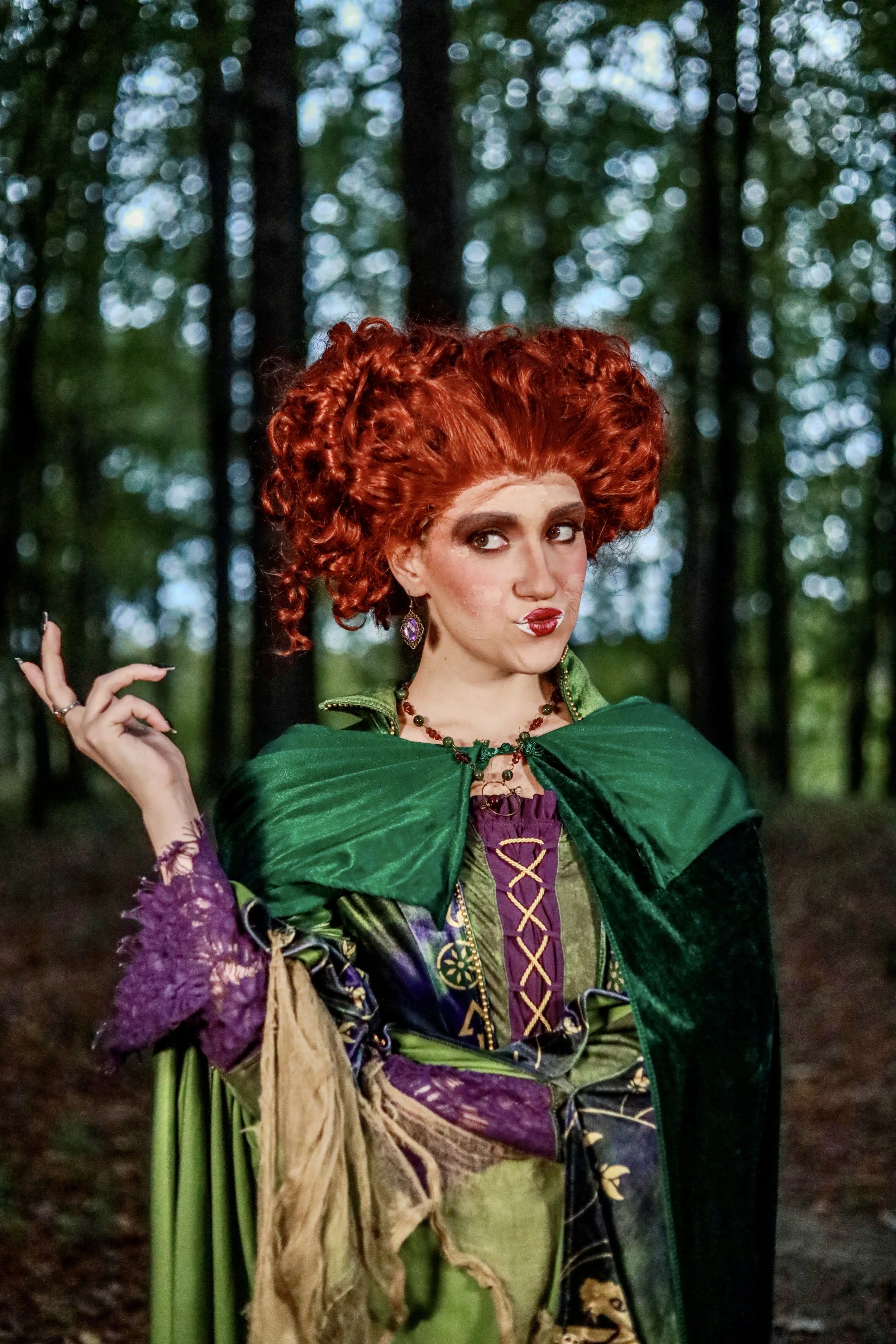 Red-haired woman in an elaborate green and purple costume posing in a forest