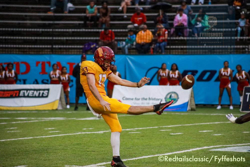 American football player in yellow uniform and helmet kicking a football during an indoor game