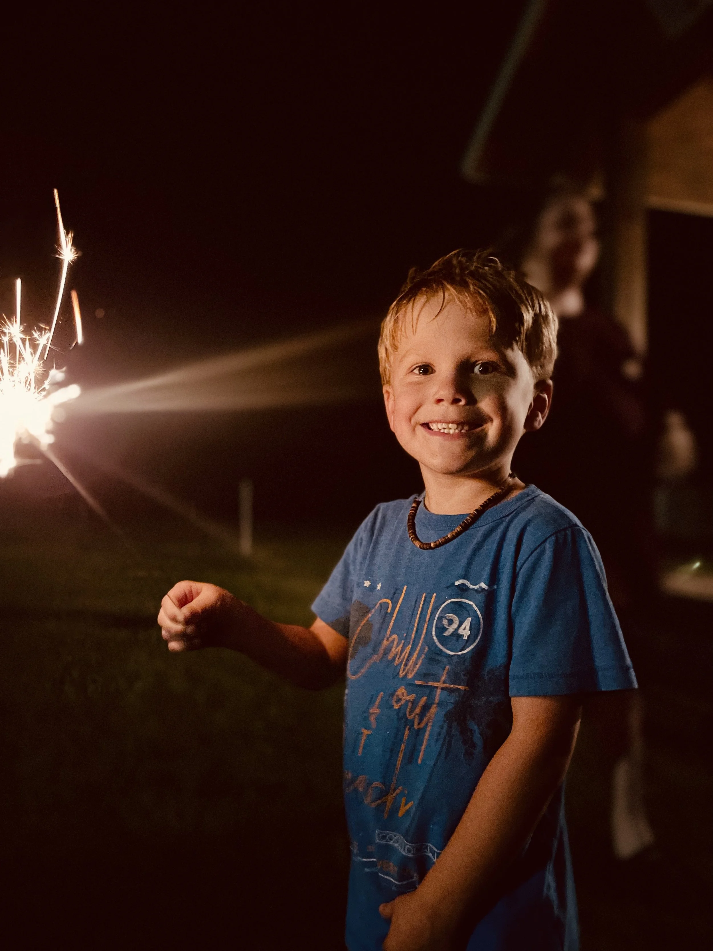 Smiling boy in a blue T-shirt holding a lit sparkler at night