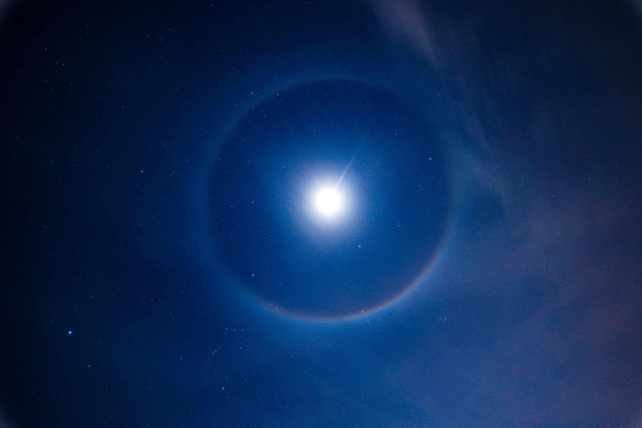 Bright full moon surrounded by stars and a circular halo in a deep blue night sky