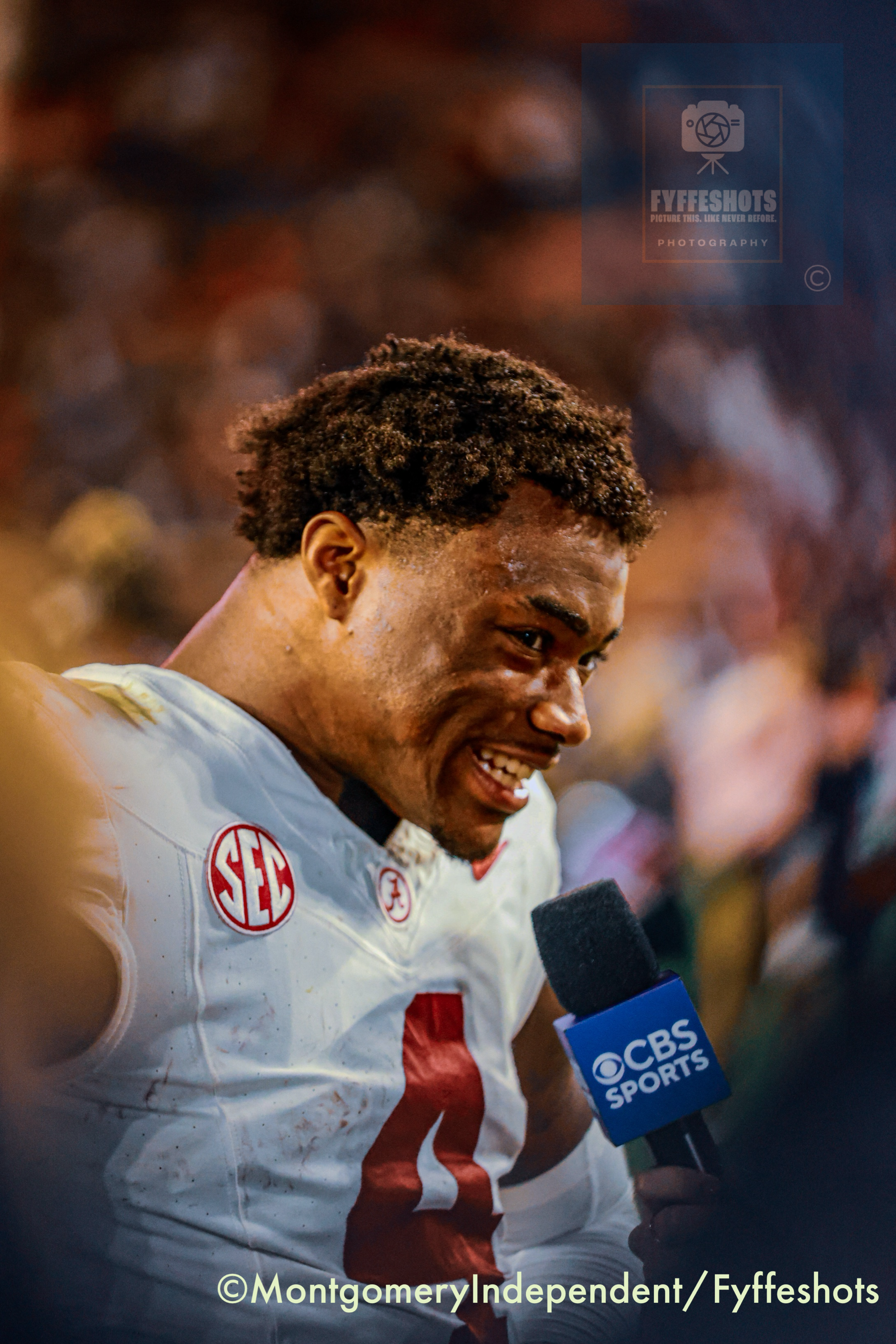Alabama football player in a white uniform speaking into a CBS Sports microphone after a game.