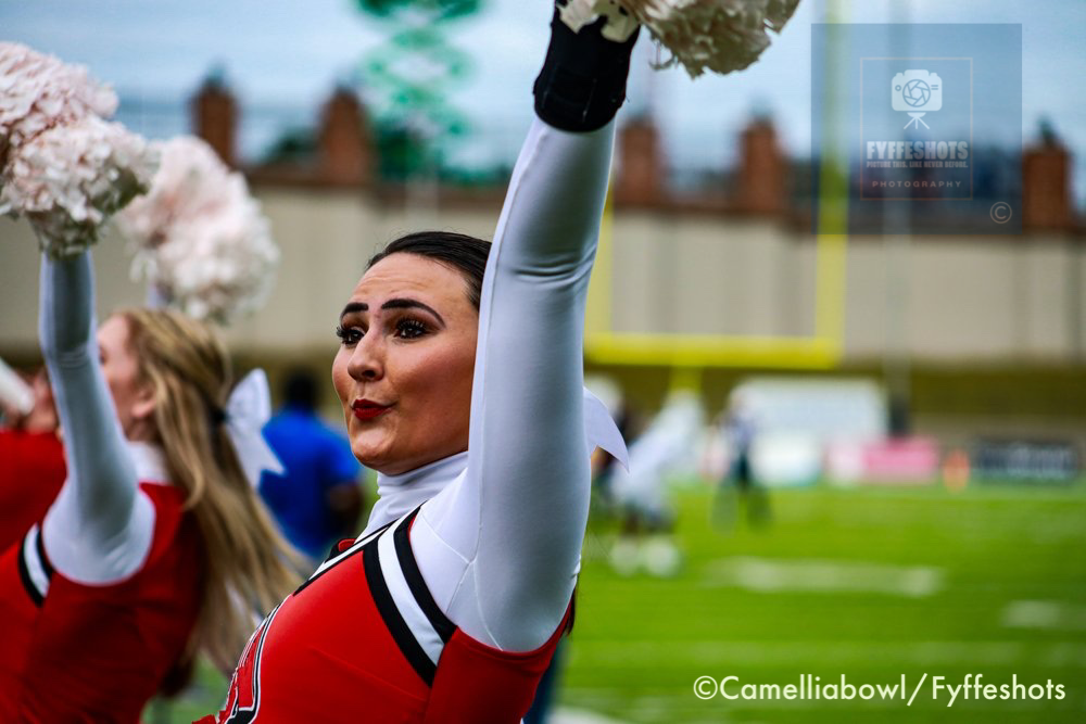 Female cheerleaders in red uniforms raising pom-poms at a football stadium