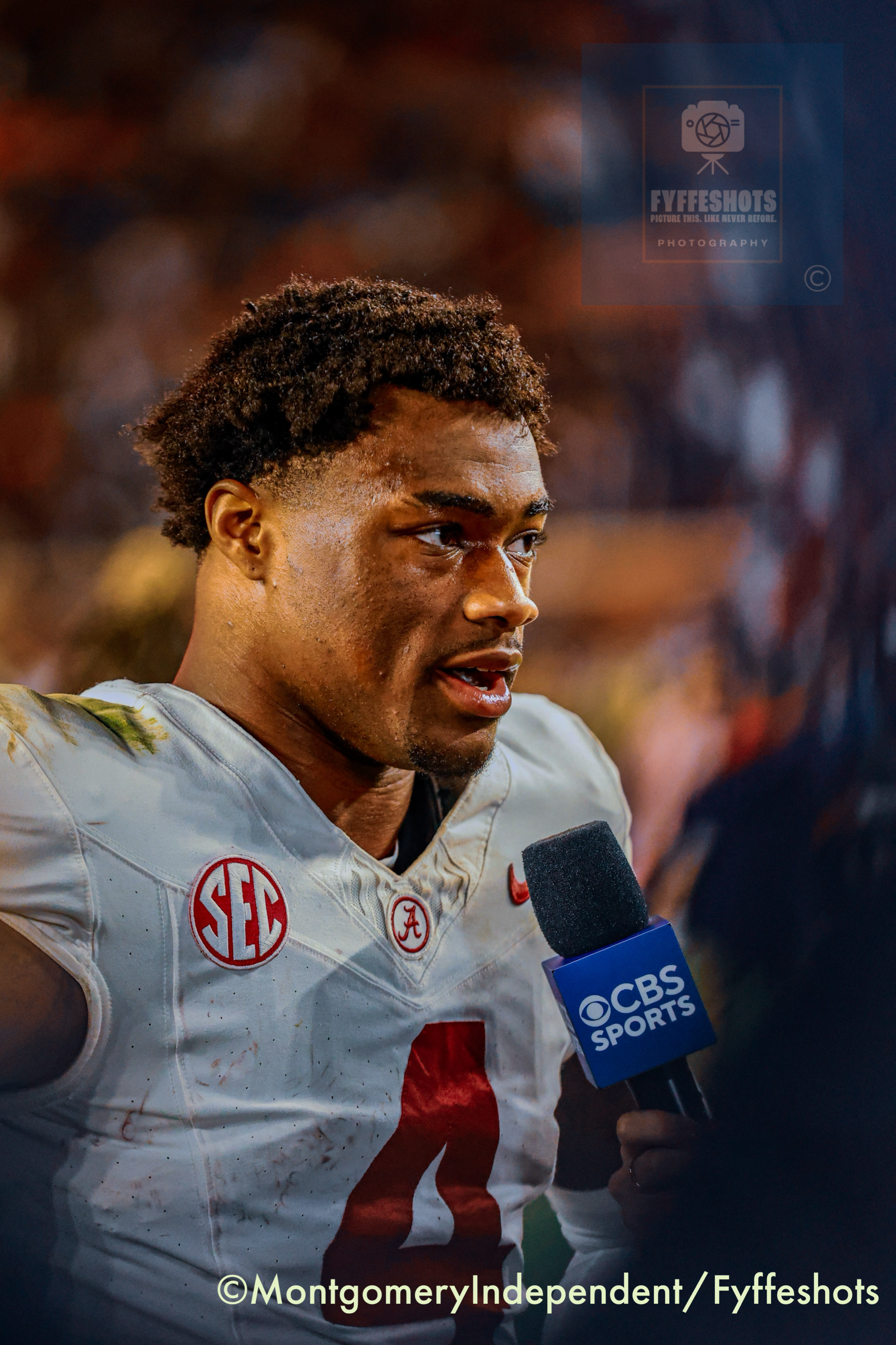 Alabama football player in a stained white uniform speaks into a CBS Sports microphone after a game.