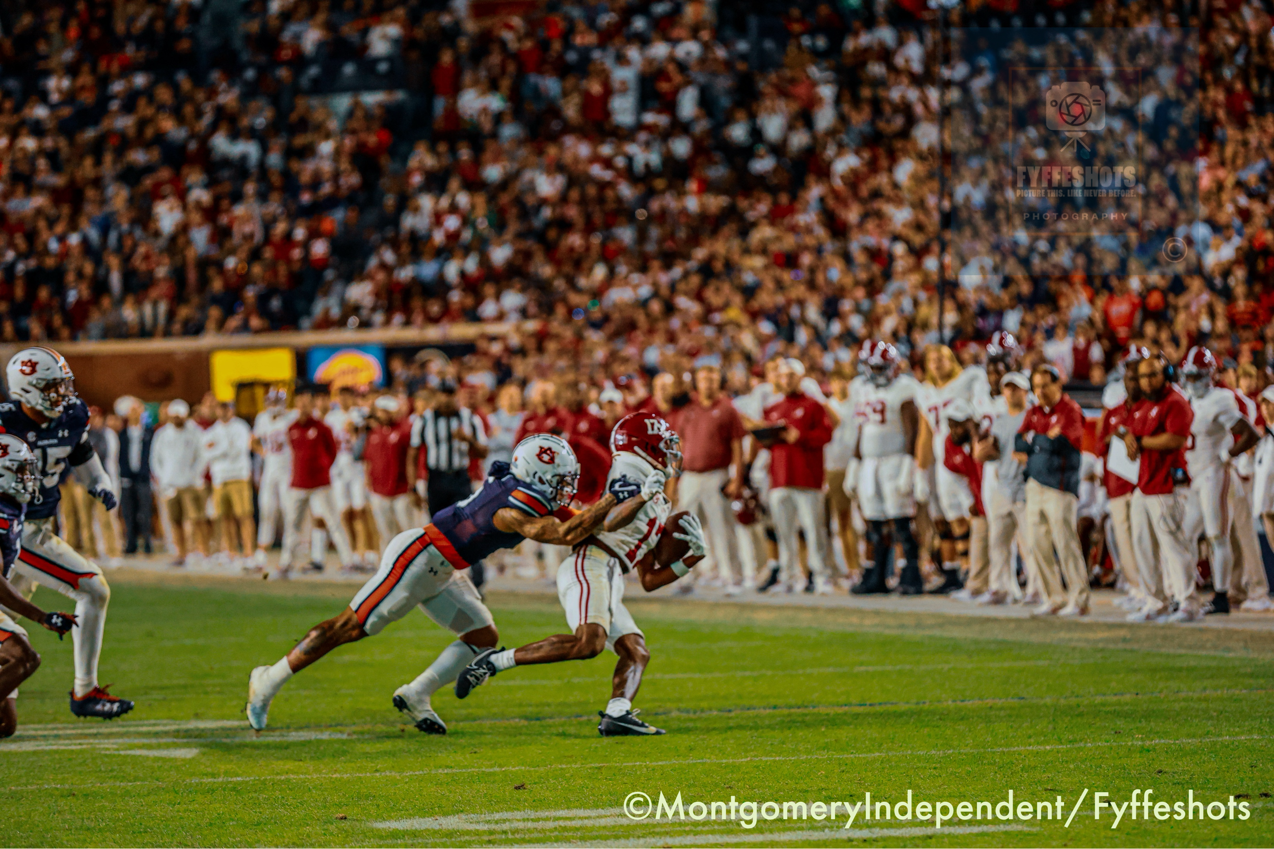 Auburn football player tackles an Alabama ball carrier during a game in front of a packed stadium crowd.