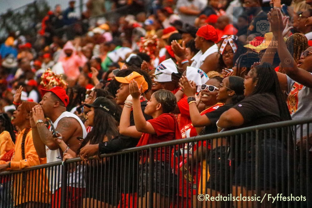 Energetic crowd of sports fans cheering and raising their hands in stadium bleachers.