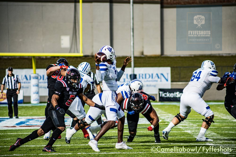 Ball State football quarterback throws a pass against opposing defenders during a college football game.