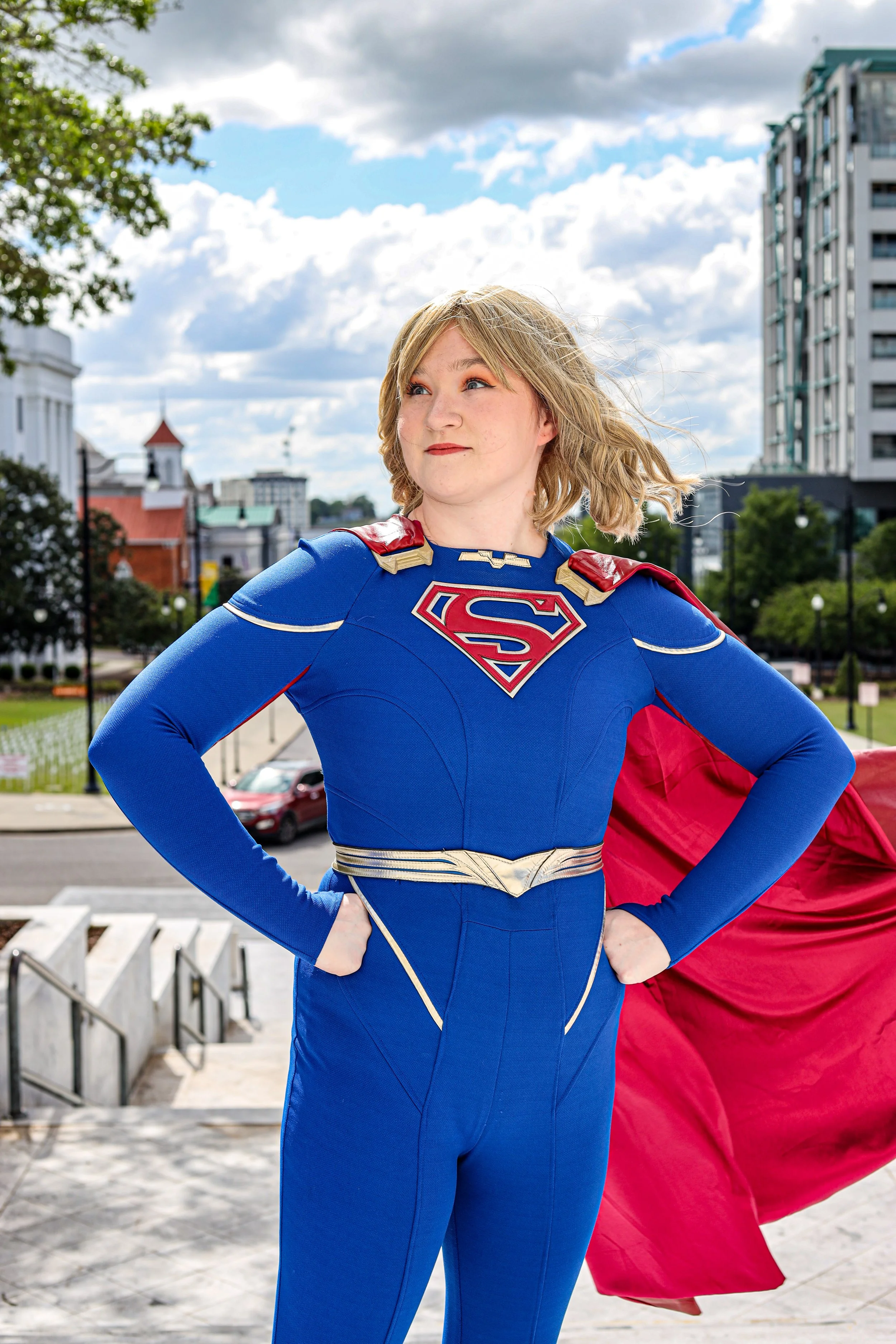 Woman in a blue and red superhero costume posing with hands on hips in an urban park