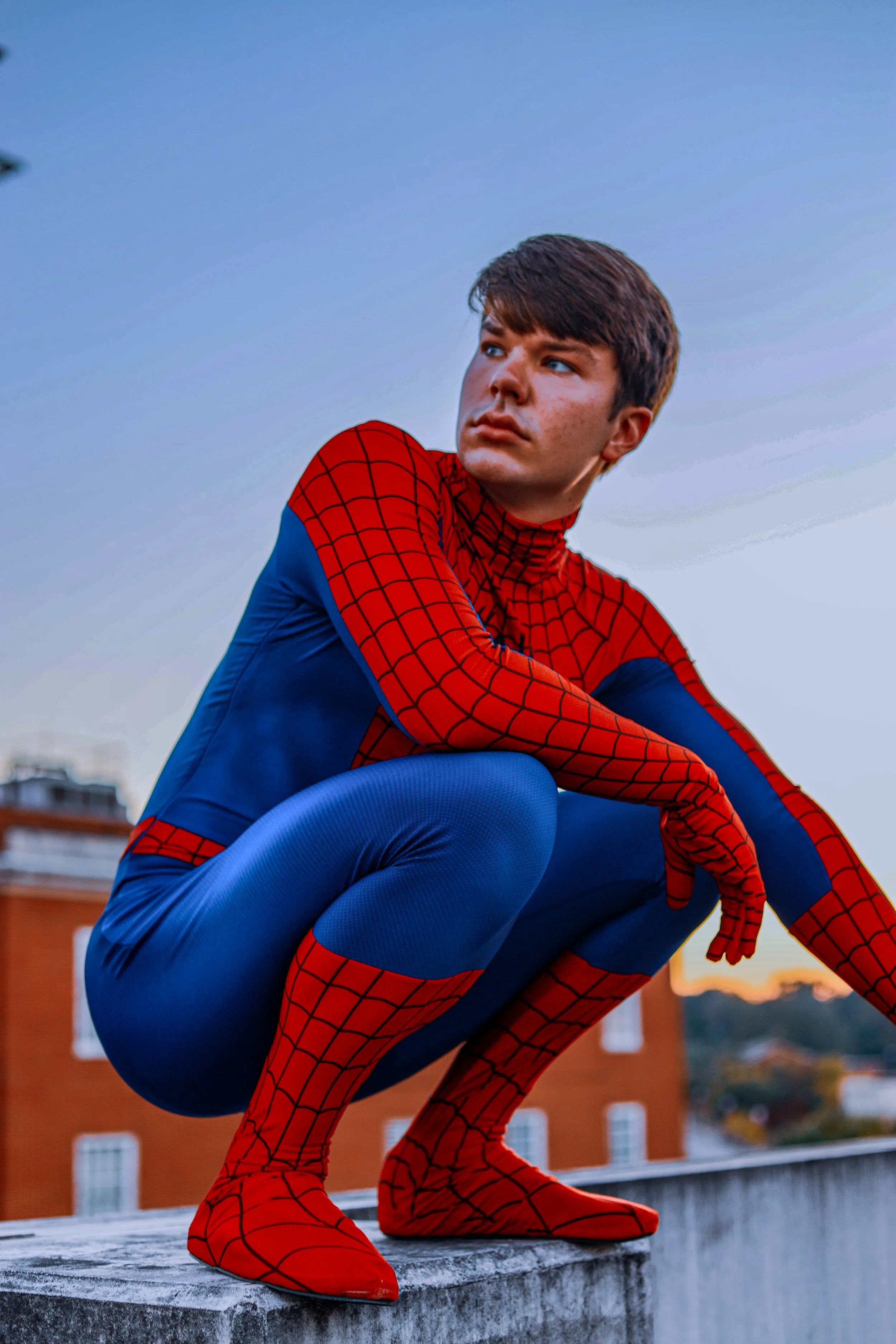 Person in a red-and-blue Spider-Man costume crouching on a rooftop ledge